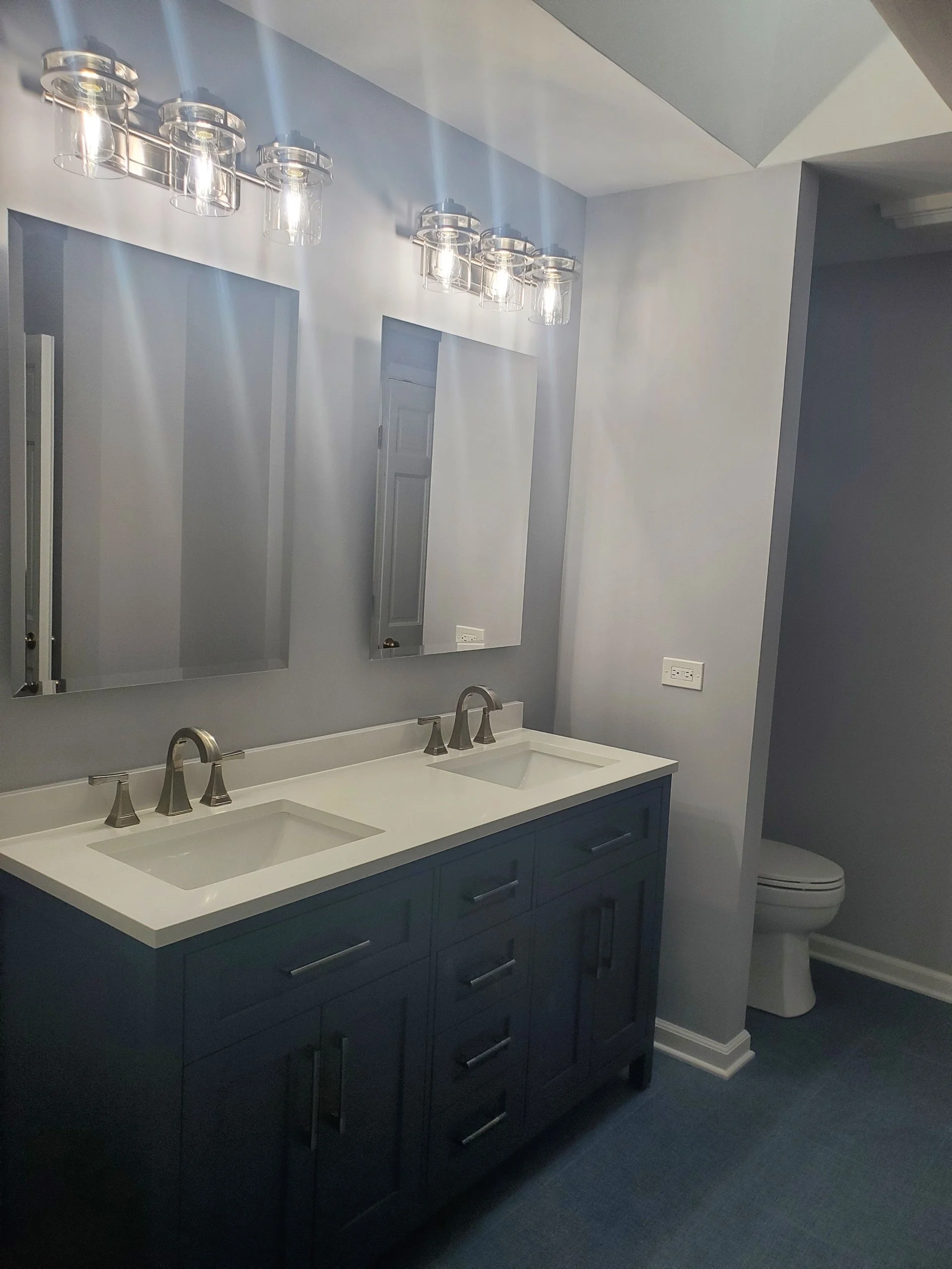 Modern bathroom with a double sink vanity, two mirrors, and a toilet in the background.