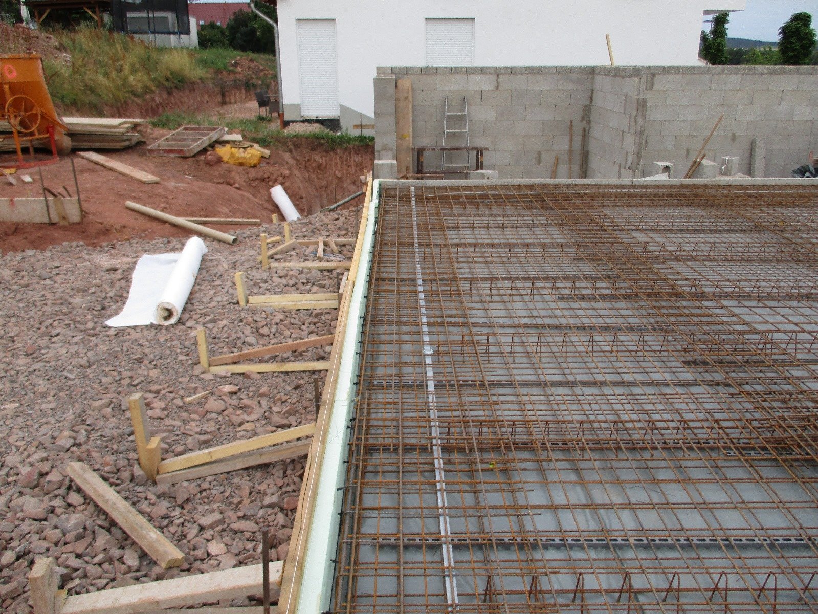 Baustelle mit Stahlbewehrung für eine Betonplatte, umgeben von Gerüst und Baumaterialien