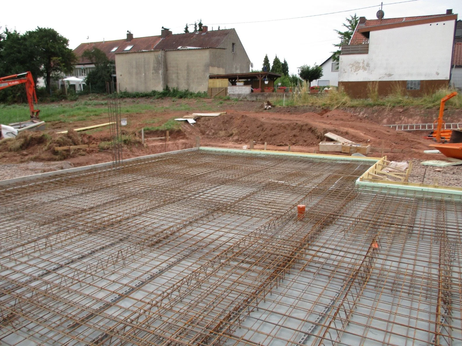 Baustelle mit sichtbarem Stahlbeton-Reinforcement für eine Bodenplatte, umgeben von Erde und Bauwerkzeugen.