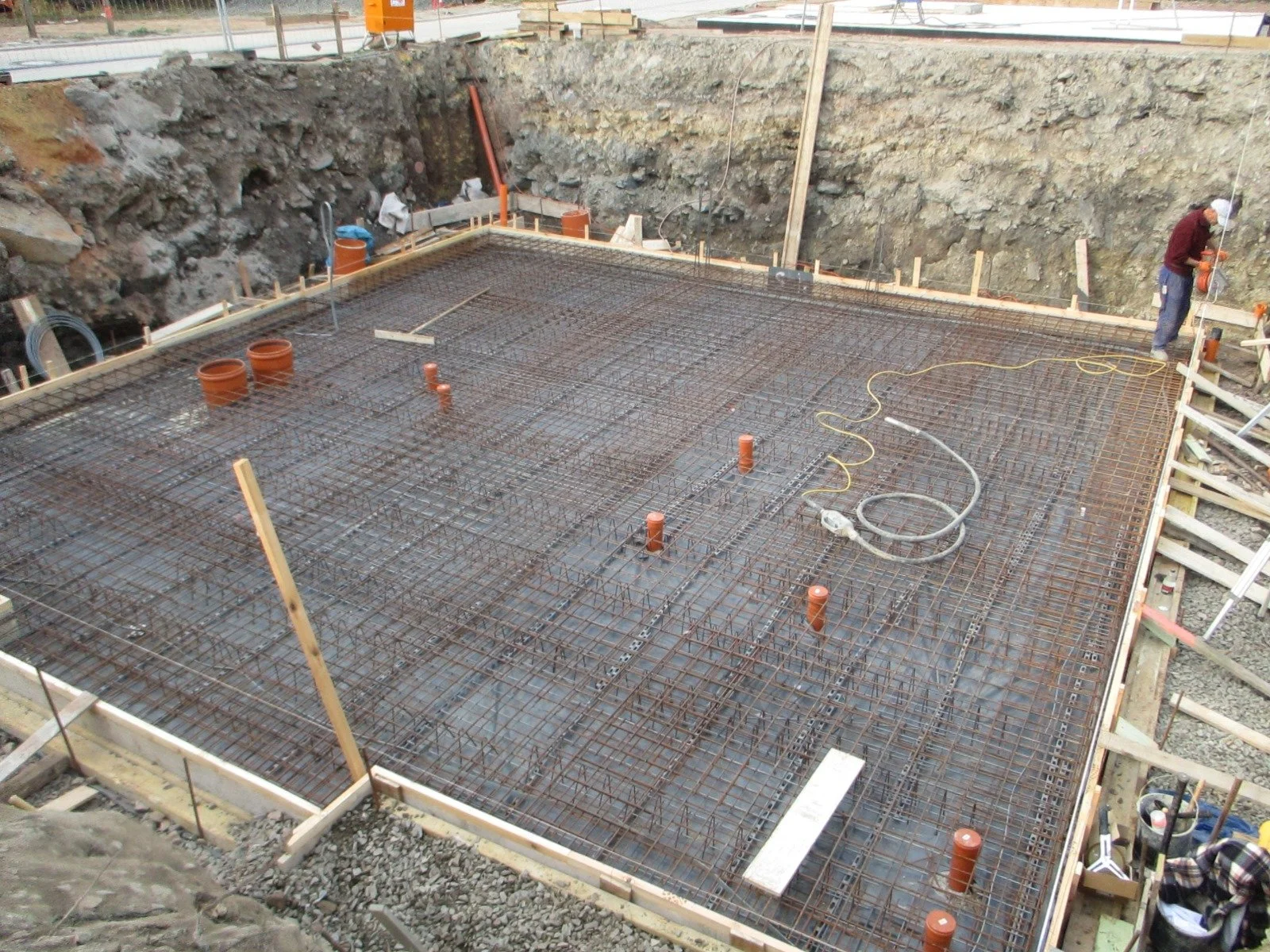Baustelle mit Eisenarmierung für eine Betondecke, zwei Rohre, und Bauarbeiter im Hintergrund.