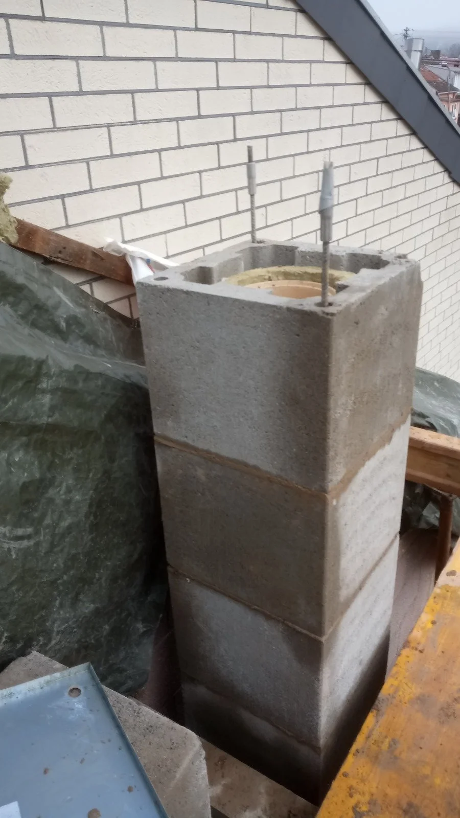 Kaminmauer aus Ziegeln im Bau, mit Betonsockel und Stahldübeln, auf einer Baustelle im Dachgeschoss.