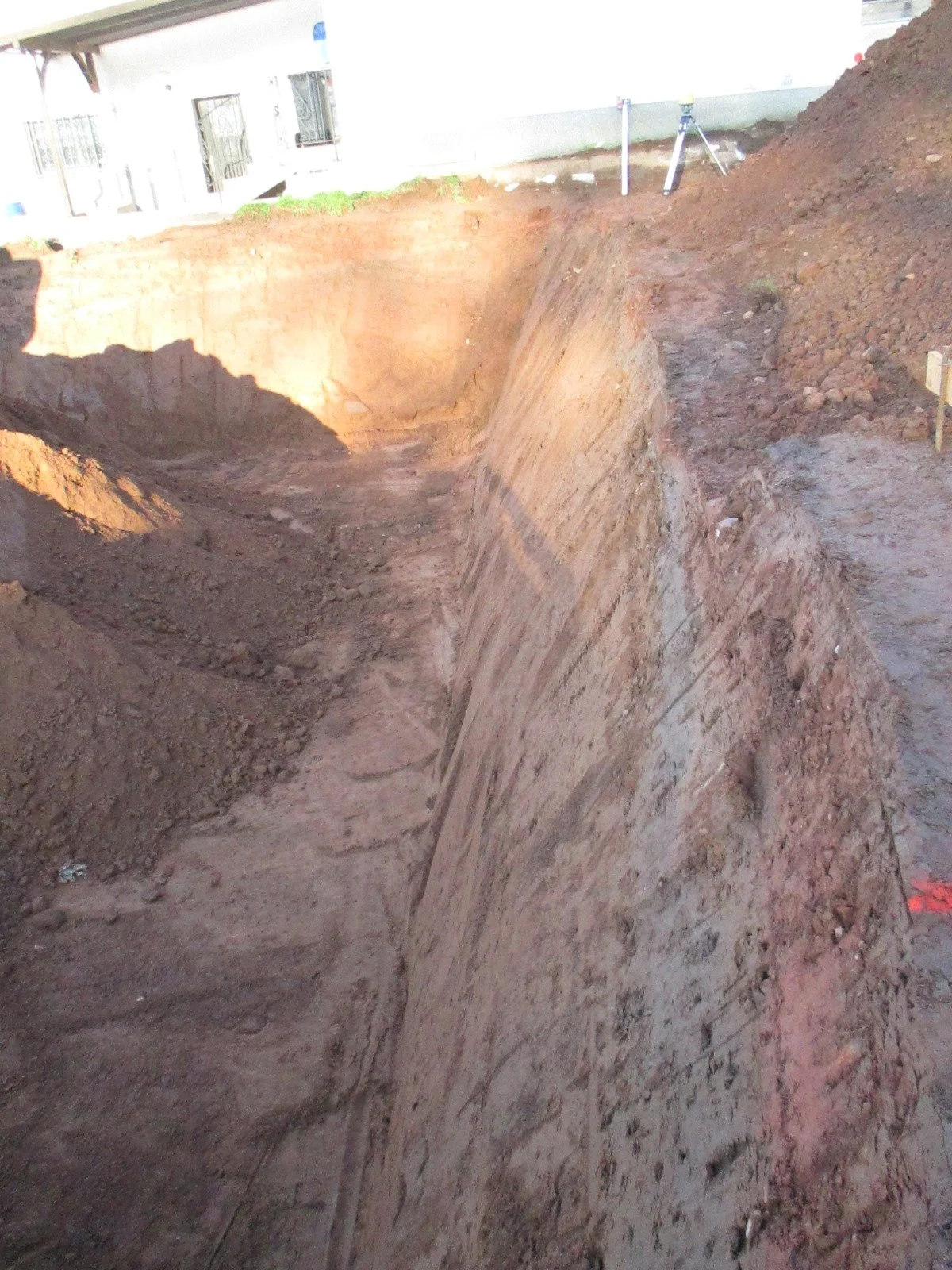 Aushubgrube mit geologischen Schichten und Vermessungsgerät auf dem Boden in einem Baugrundstück.
