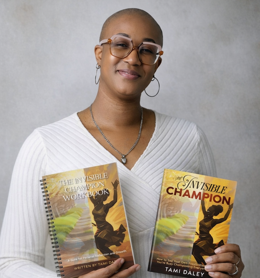 Tamica Daley with glasses and hoop earrings holding her workbook titled "The Invisible Champion Workbook" and her book titled "The Invisible Champion" by Tami Daley, smiling at the camera.
