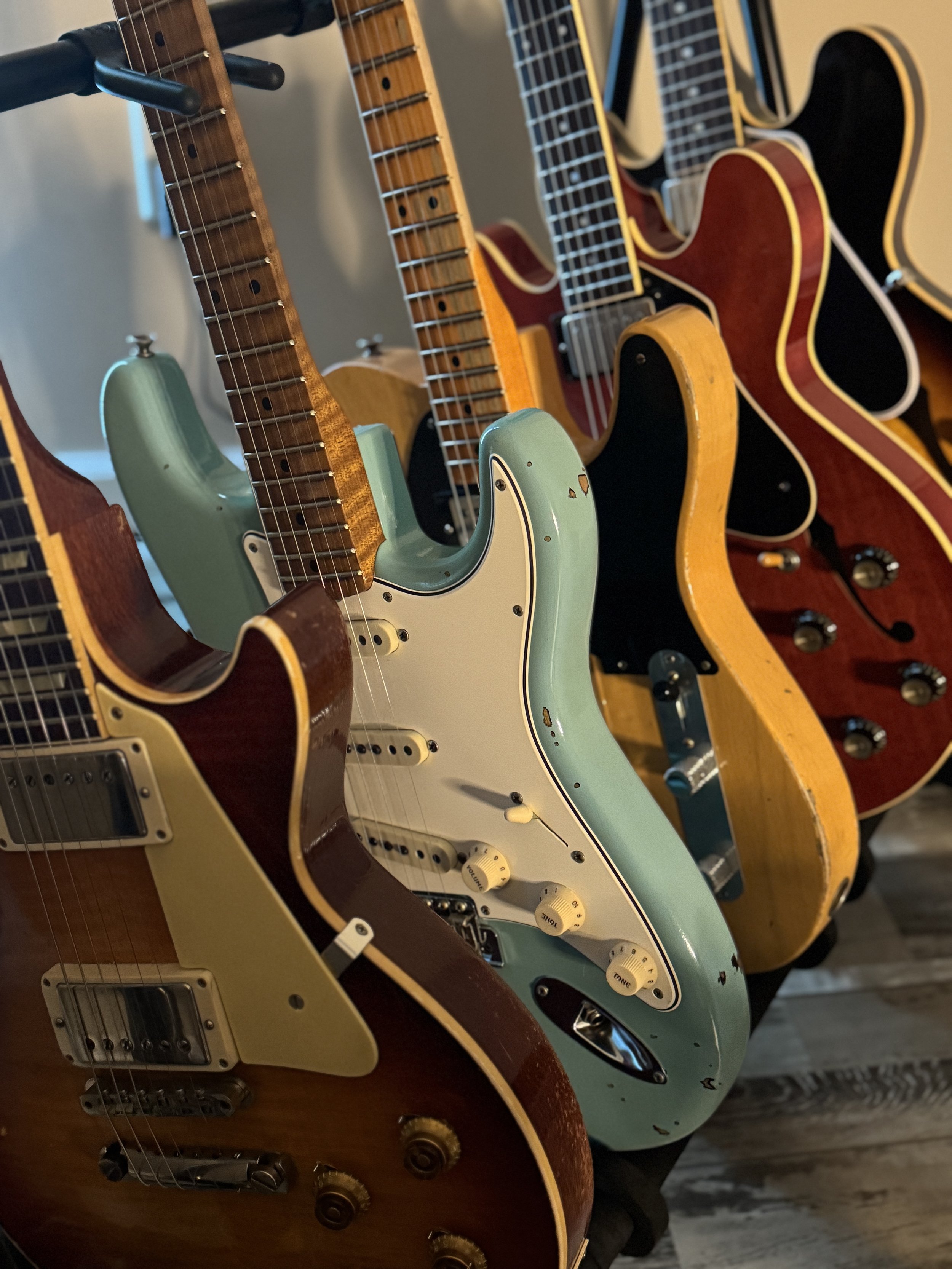 A display of vintage electric and acoustic guitars hanging on a wall, featuring various colors and styles.