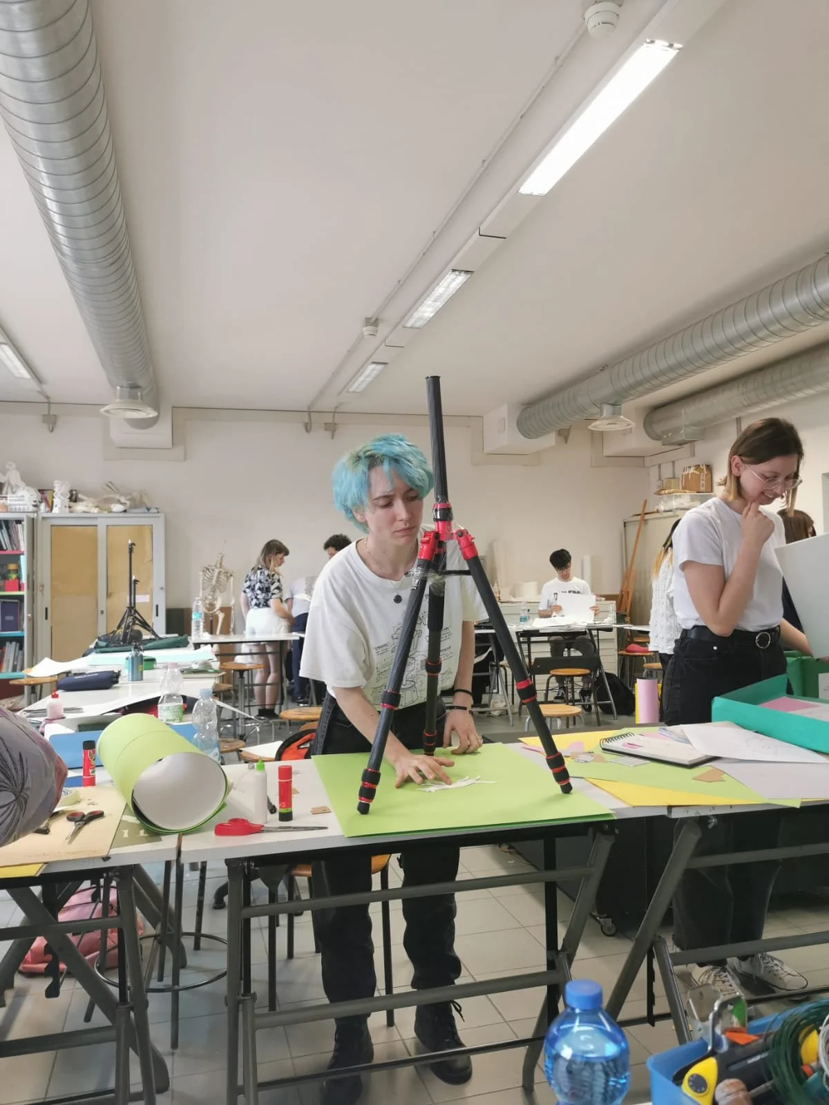 Studente con capelli tinti di blu che lavora con una macchina fotografica tripod su un tavolo in un laboratorio scolastico.