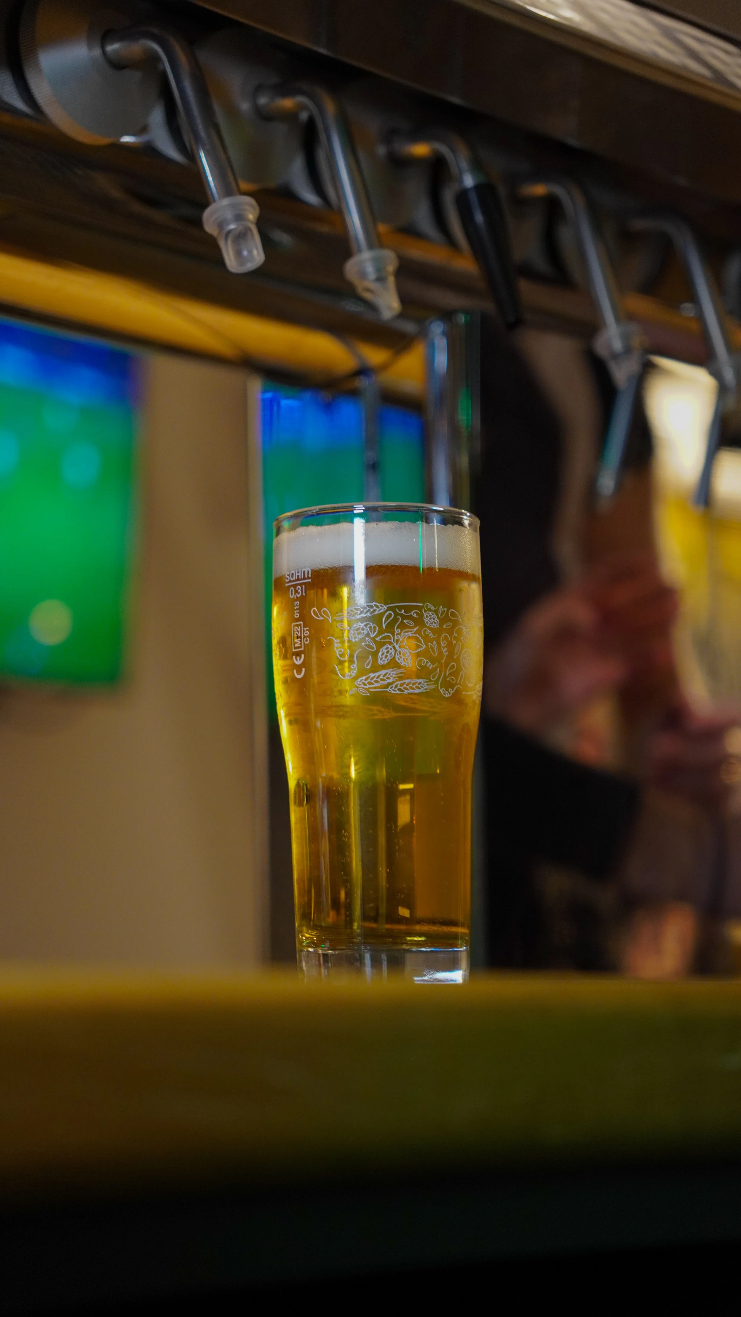 Verre de bière dorée avec mousse sur une table, dans un environnement de bar ou restaurant.