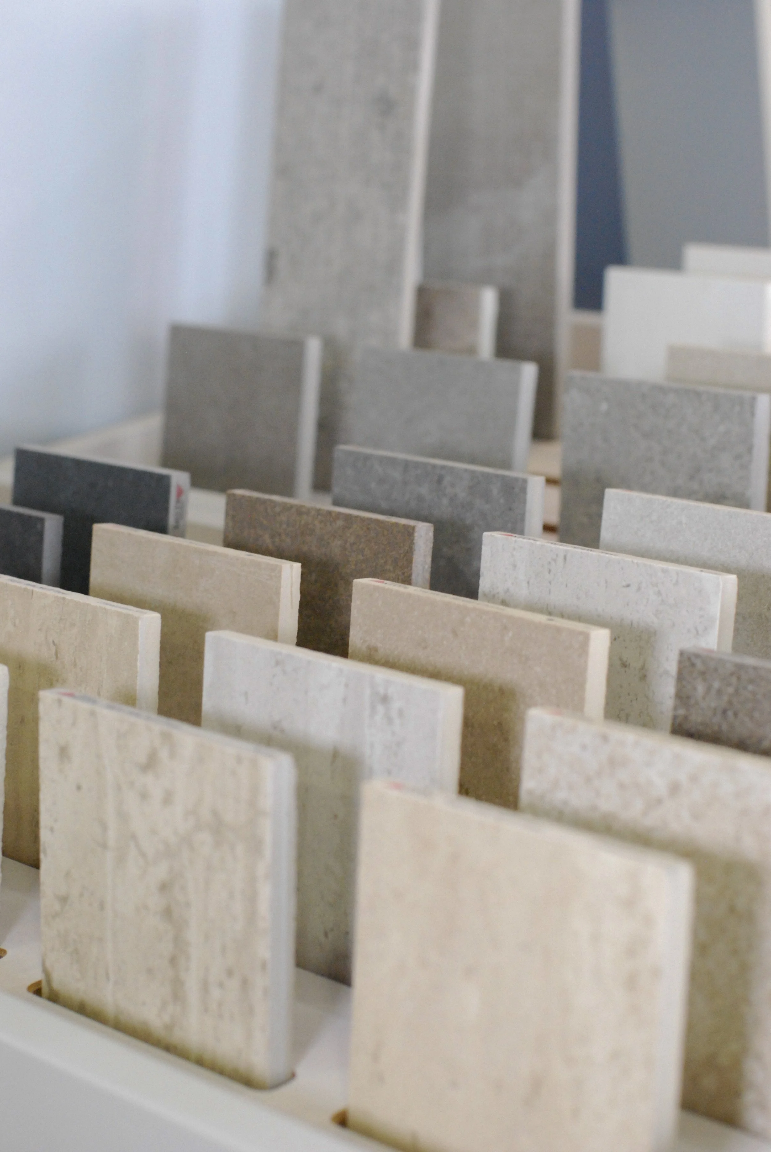 Échantillons de carreaux de différentes couleurs et textures, disposés en rangées sur une table, utilisés pour la sélection de revêtements de sol ou muraux.