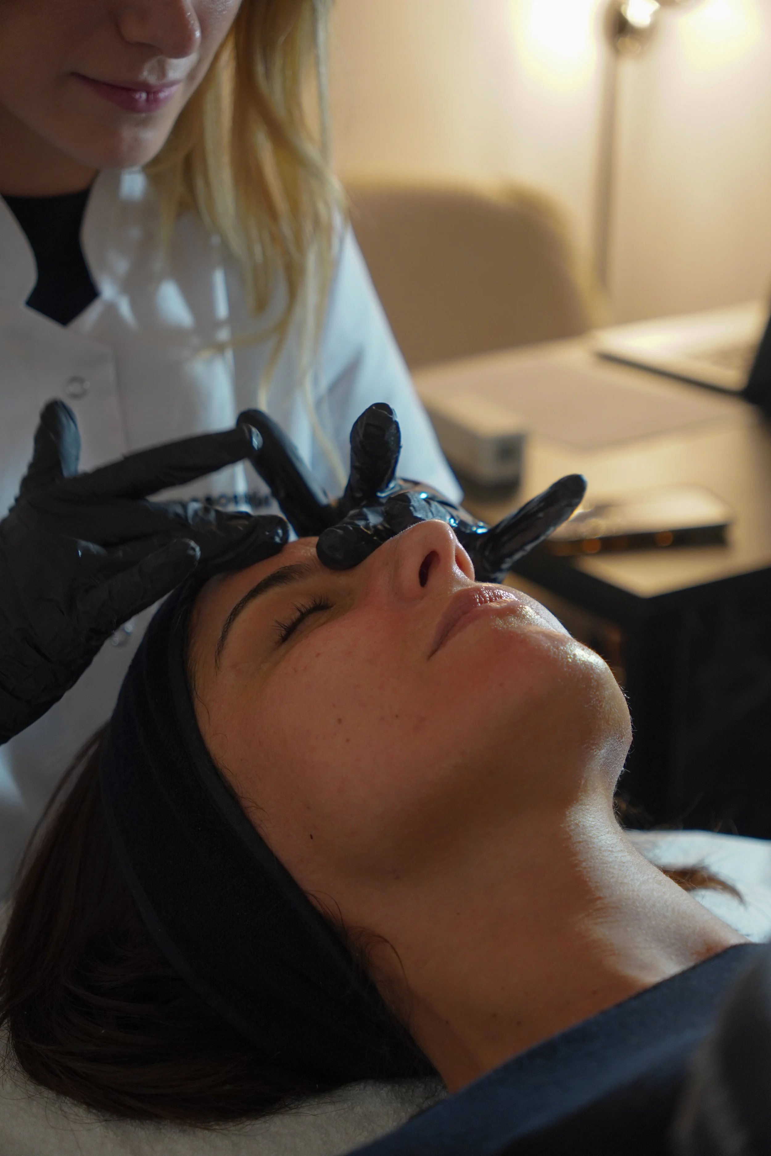 Une esthéticienne effectuant un soin du visage sur une cliente allongée, dans un environnement de spa ou de salon de beauté.