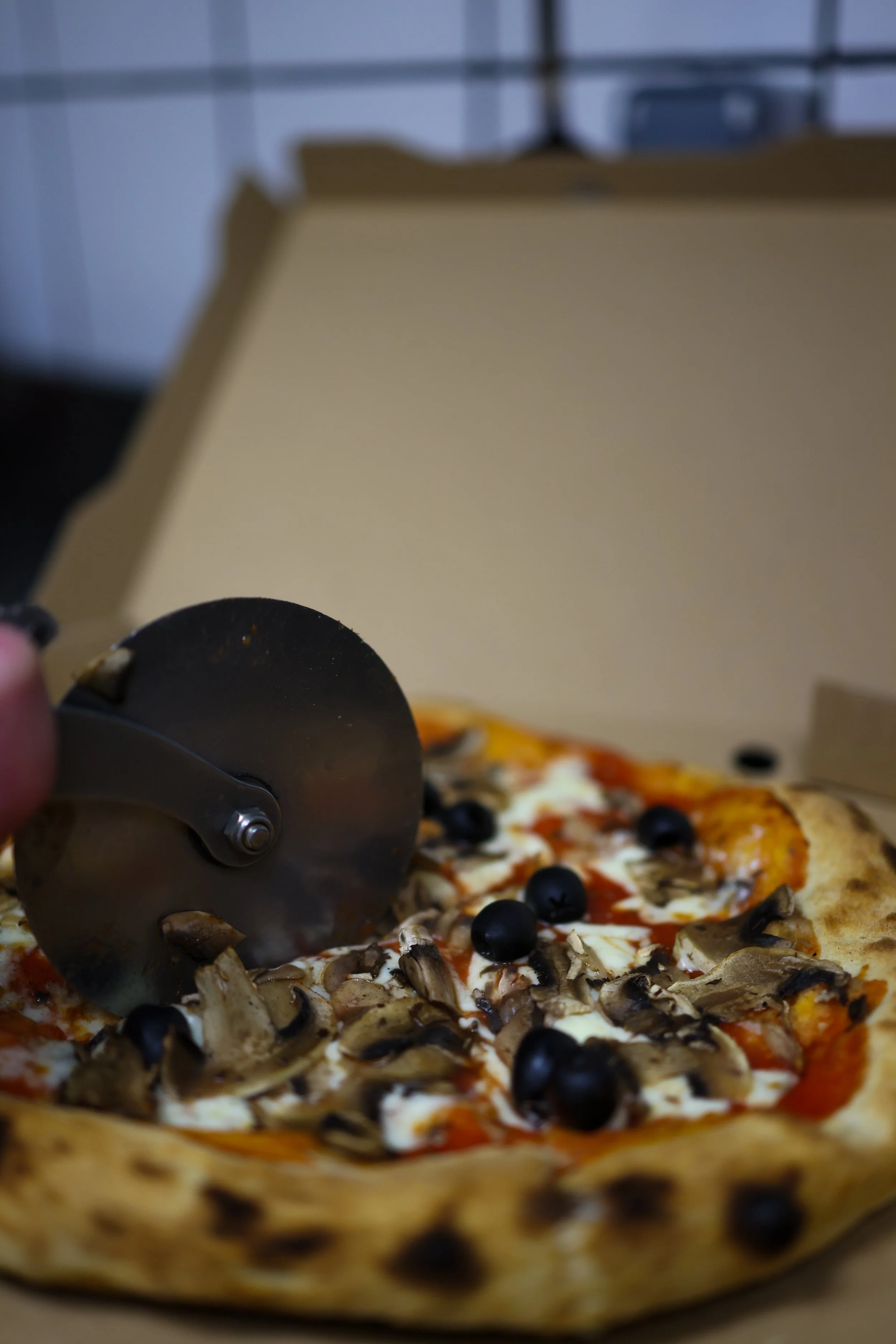 Une pizza dans une boîte en carton avec des champignons, des olives noires, et de la mozzarella, ready to be slice.