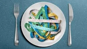 A white plate with tangled colorful measuring tapes, placed on a blue surface with a fork and knife on the sides.