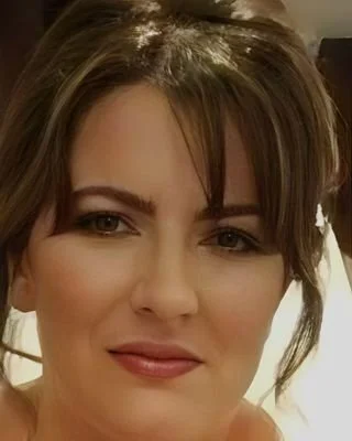 Close-up of a woman with brown hair and makeup, smiling softly.