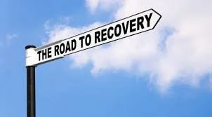 Street sign reading 'The Road to Recovery' against a blue sky with clouds.