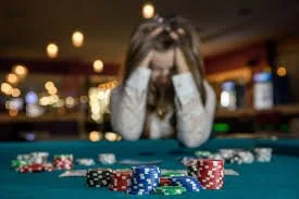 A woman sitting at a poker table with her head in her hands, surrounded by poker chips and cards, in a casino setting.