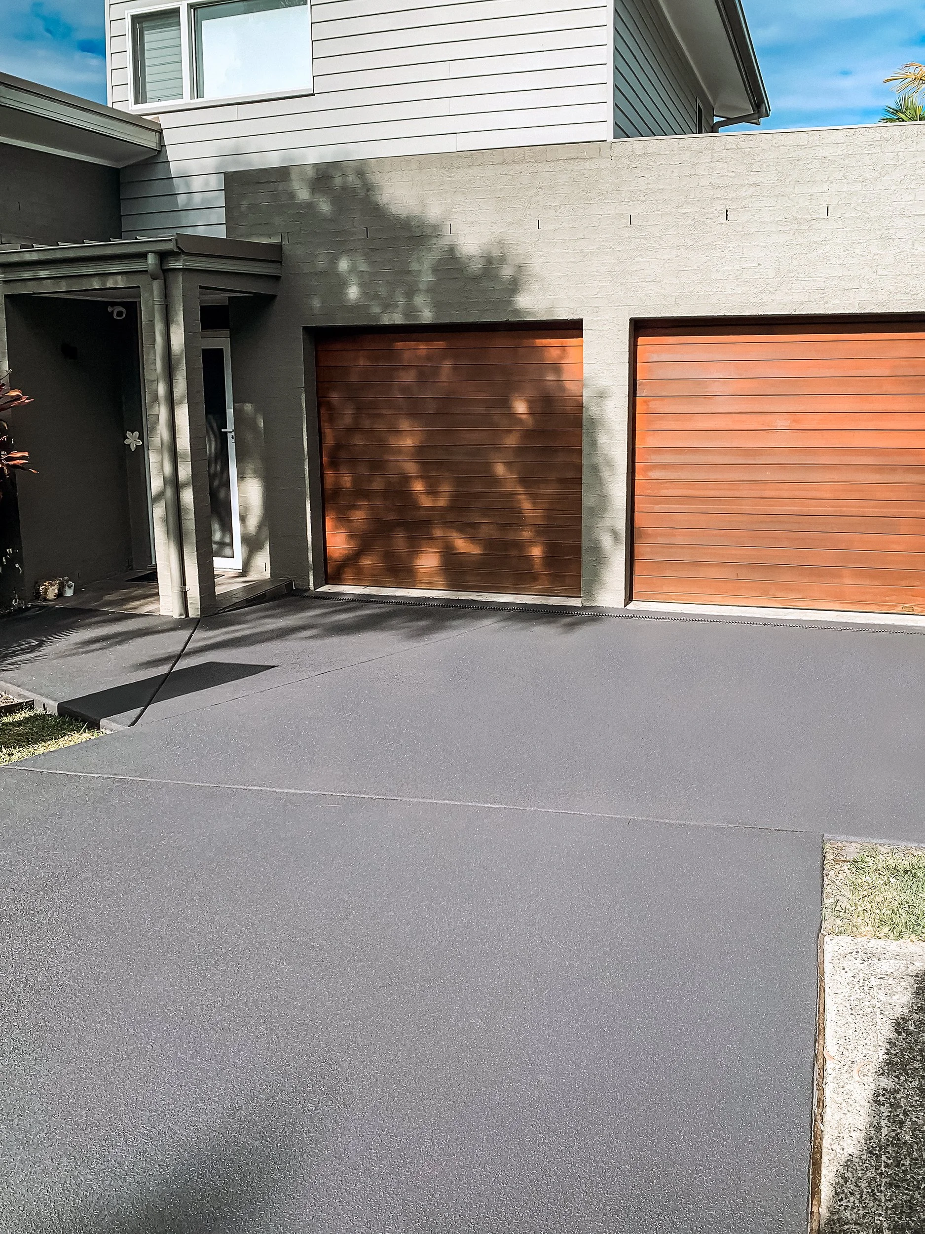concrete resurfacing and repair Warriewood northern beaches, a dark grey coloured driveway newly finished by our team using dulux avista resurfacing products, the background shows a modern suburban home with a sandy beige coloured rendered exterior