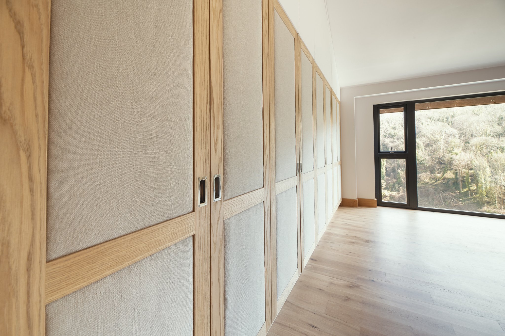 Luxury bespoke master dressing room wardrobes with pivot pocket doors and oak veneer in Dartmouth, Devon