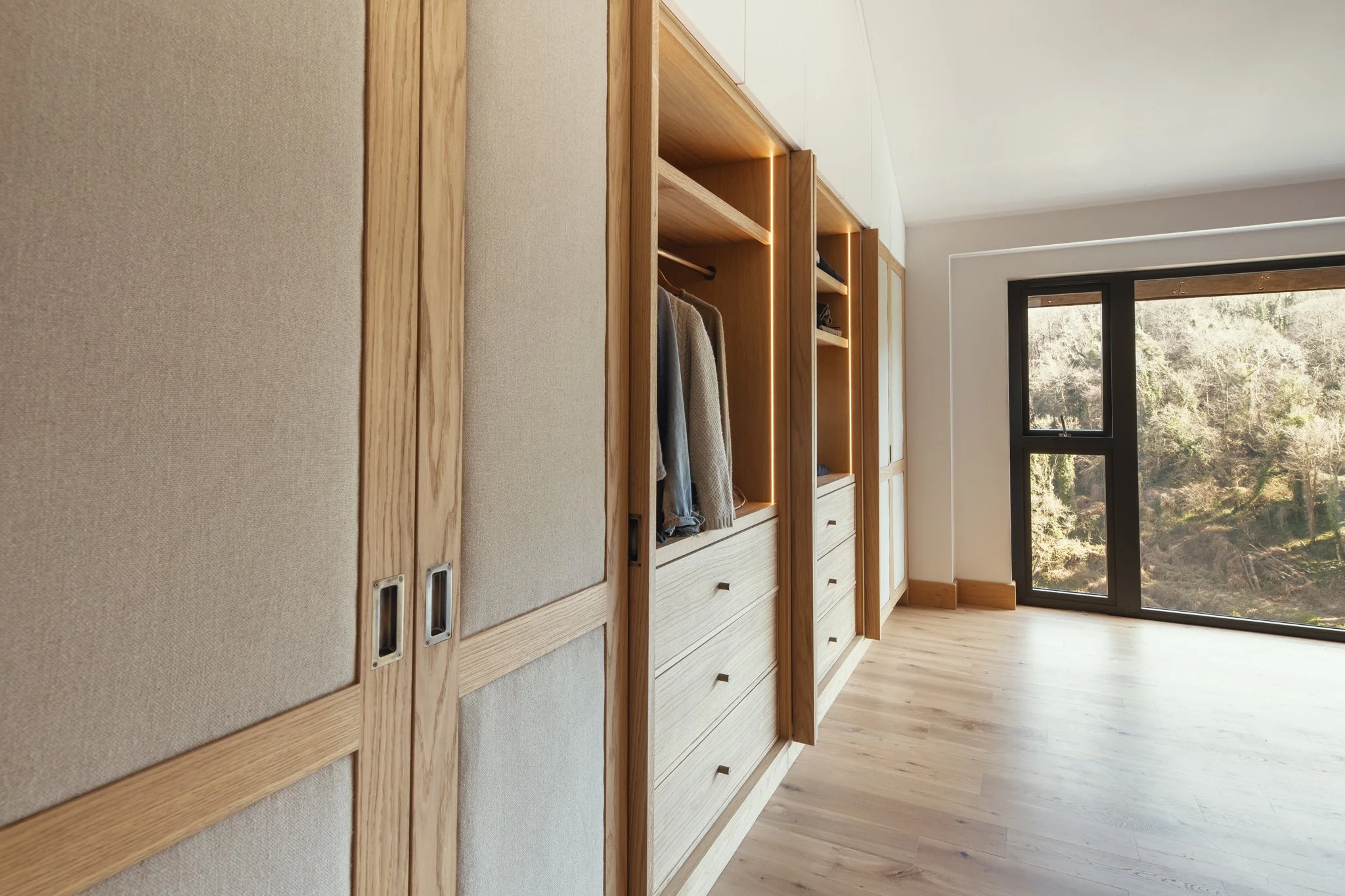 Luxury bespoke master dressing room wardrobes with pivot pocket doors and oak veneer in Dartmouth, Devon
