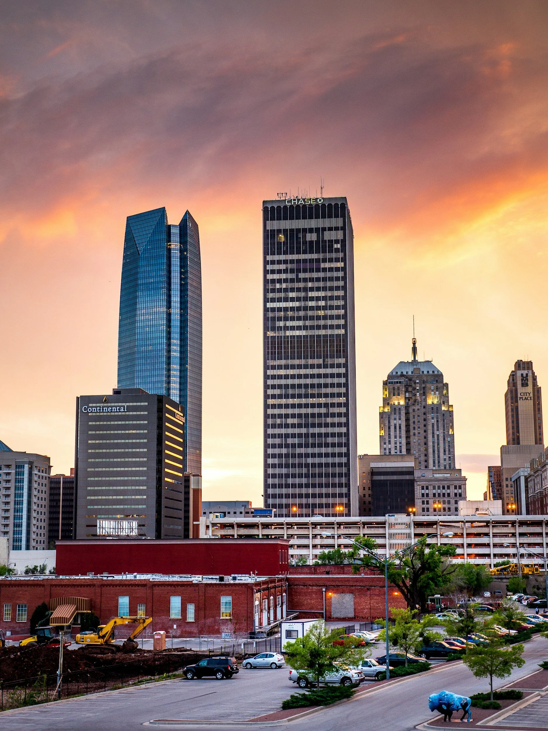 City skyline during sunset with tall modern skyscrapers, including Chase and Continental buildings, and a parking lot in the foreground.