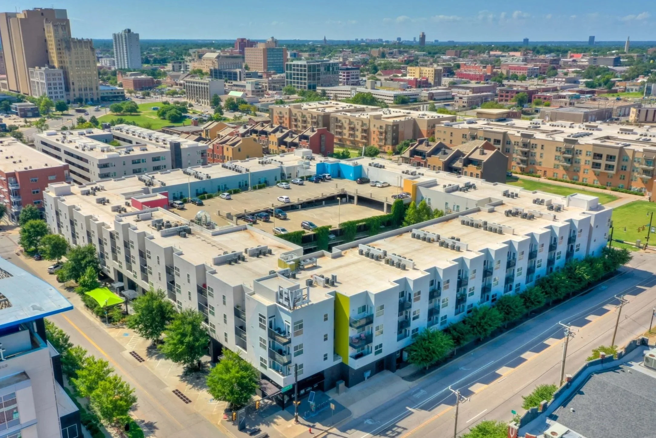 Aerial view of a modern apartment complex in an urban area, with a large parking lot and surrounding cityscape.