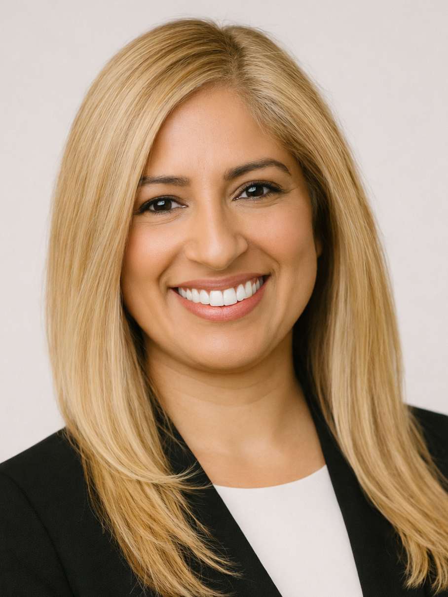 Close-up photo of a smiling woman with long blonde hair, wearing a black blazer over a white top, against a light neutral background.