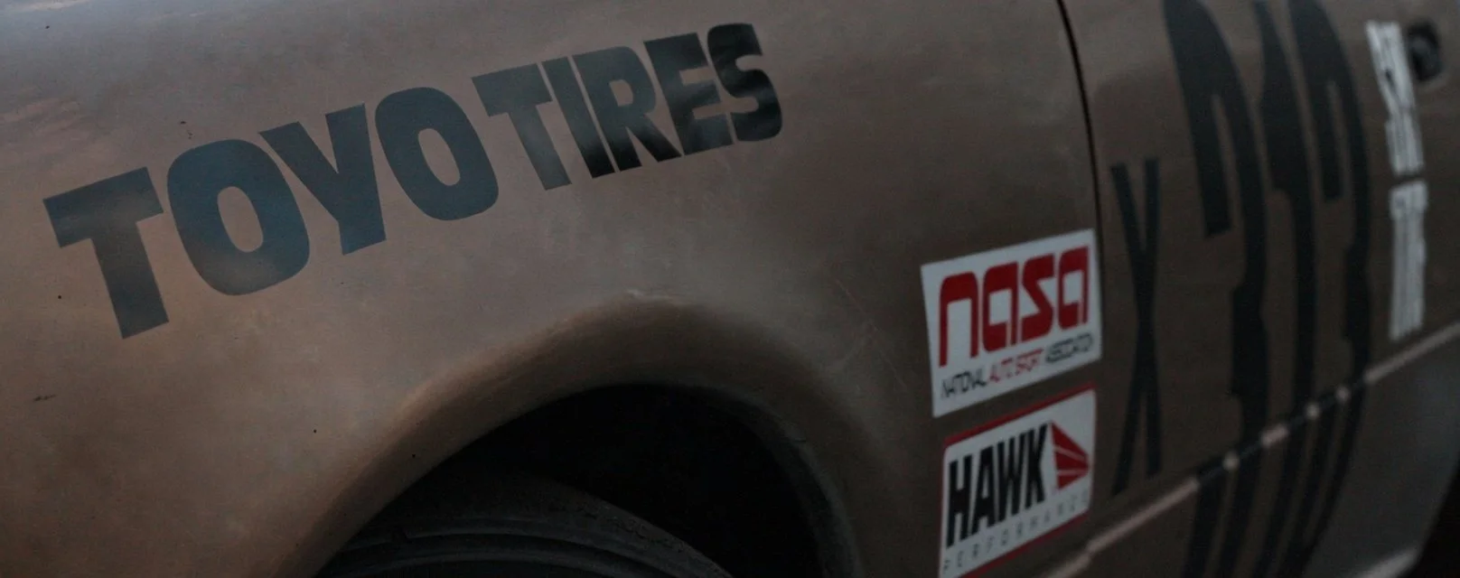 Close-up of a car door with stickers that read 'TOYOTIRES', 'NASA', and 'HAWK'.