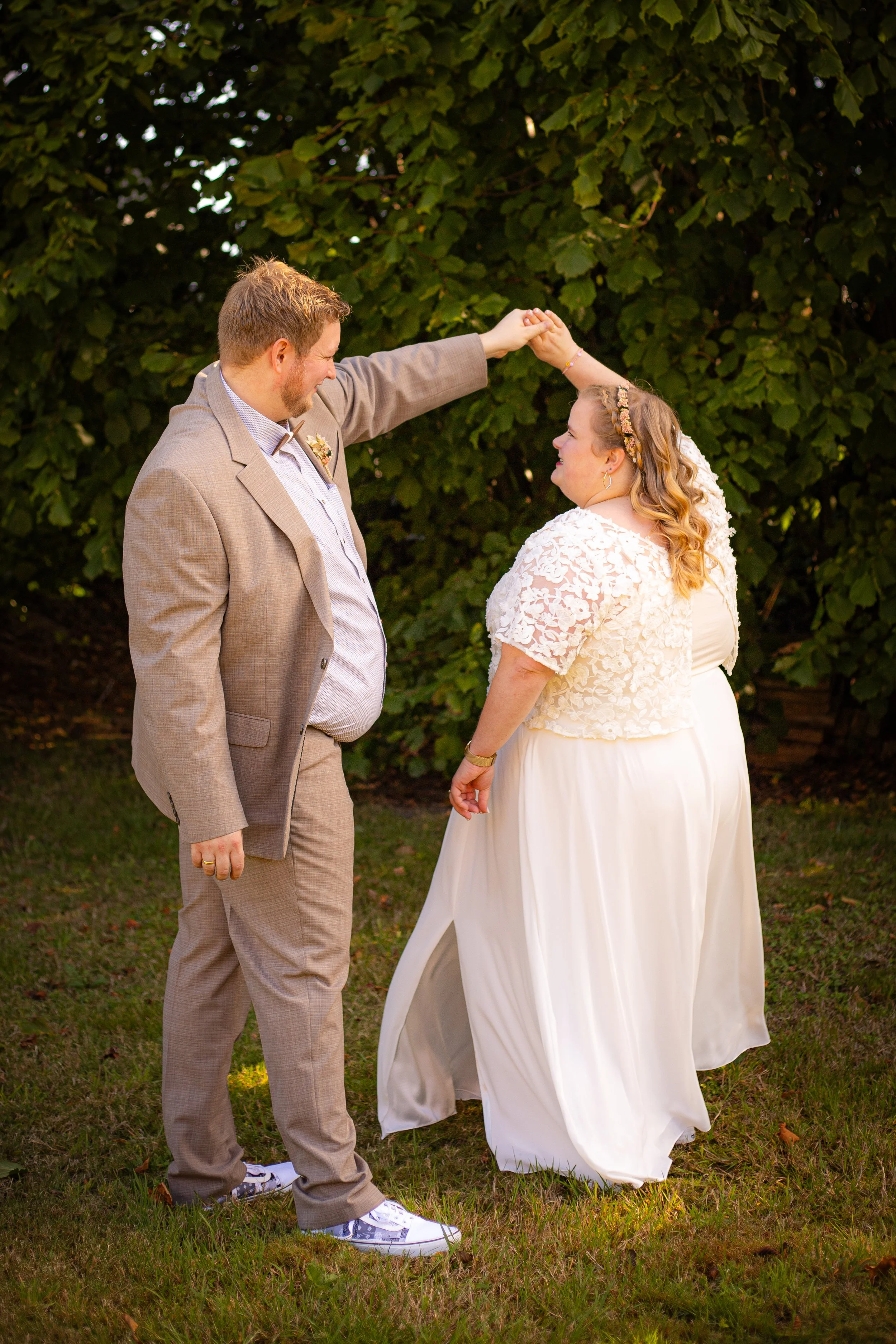 Ein Paar bei einer Hochzeit tanzt im Freien, der Mann hebt die Hand der Braut, im Hintergrund grüne Bäume.