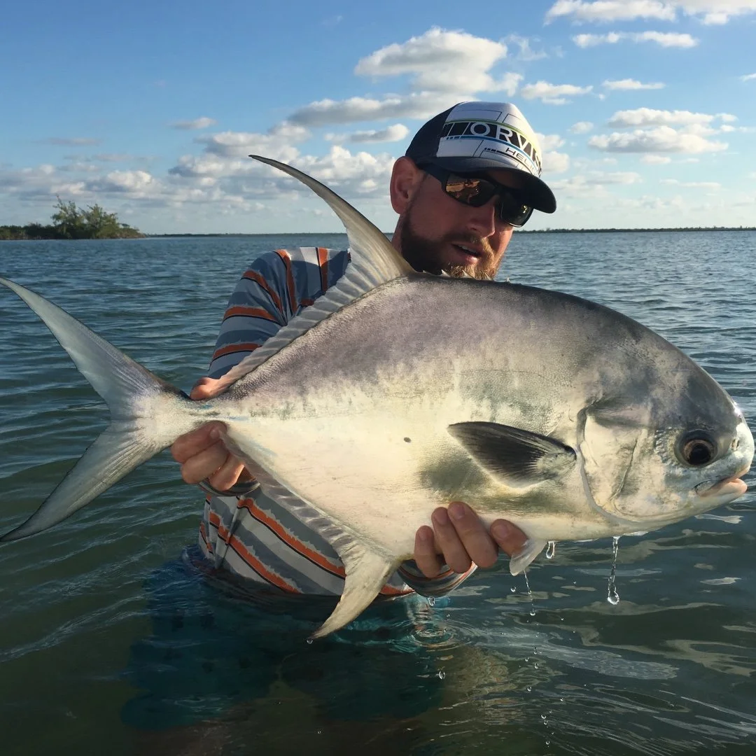 Man holding a large fish with open water and blue sky in the background.