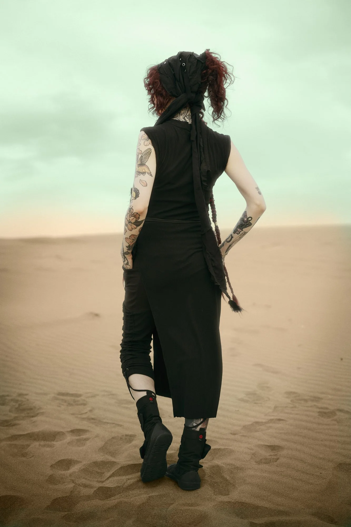 𝔄𝔦𝔫𝔥𝔬𝔞 𝔗.ℭ. standing in the desert wearing layered flowing clothing in a Dune-inspired portrait