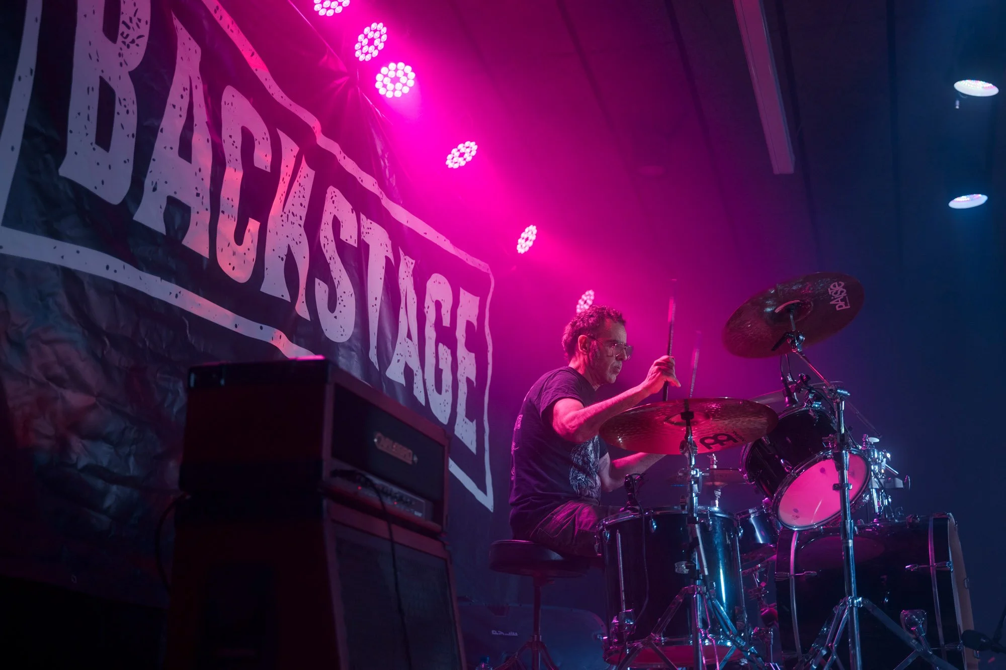 drummer playing under purple stage lights at metal concert