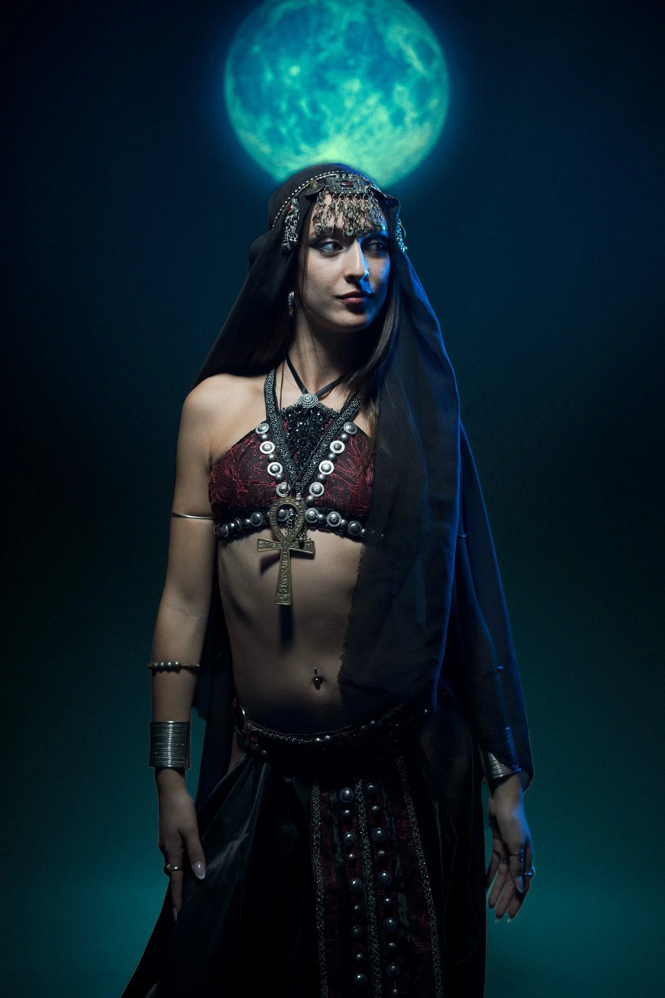 Tribal fusion dancer posing with moon projection in a dark, atmospheric studio setting.