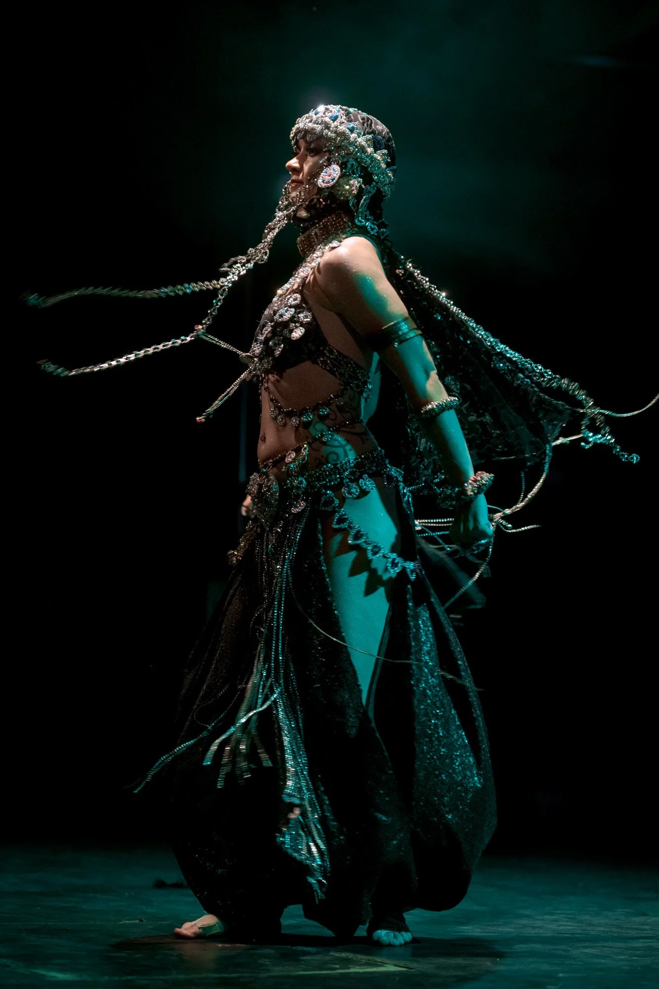 Kira Habibi Lal posing in profile under blue stage light during tribal fusion recital.