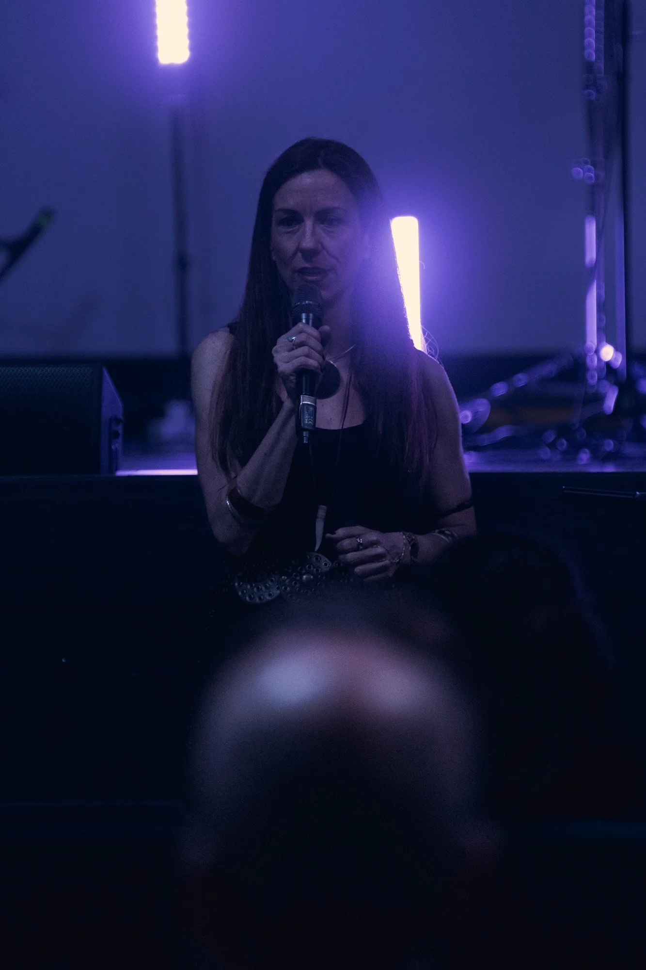 Guest artist presenting Serapis Project on stage before the concert begins, theatre setting with blue lighting.