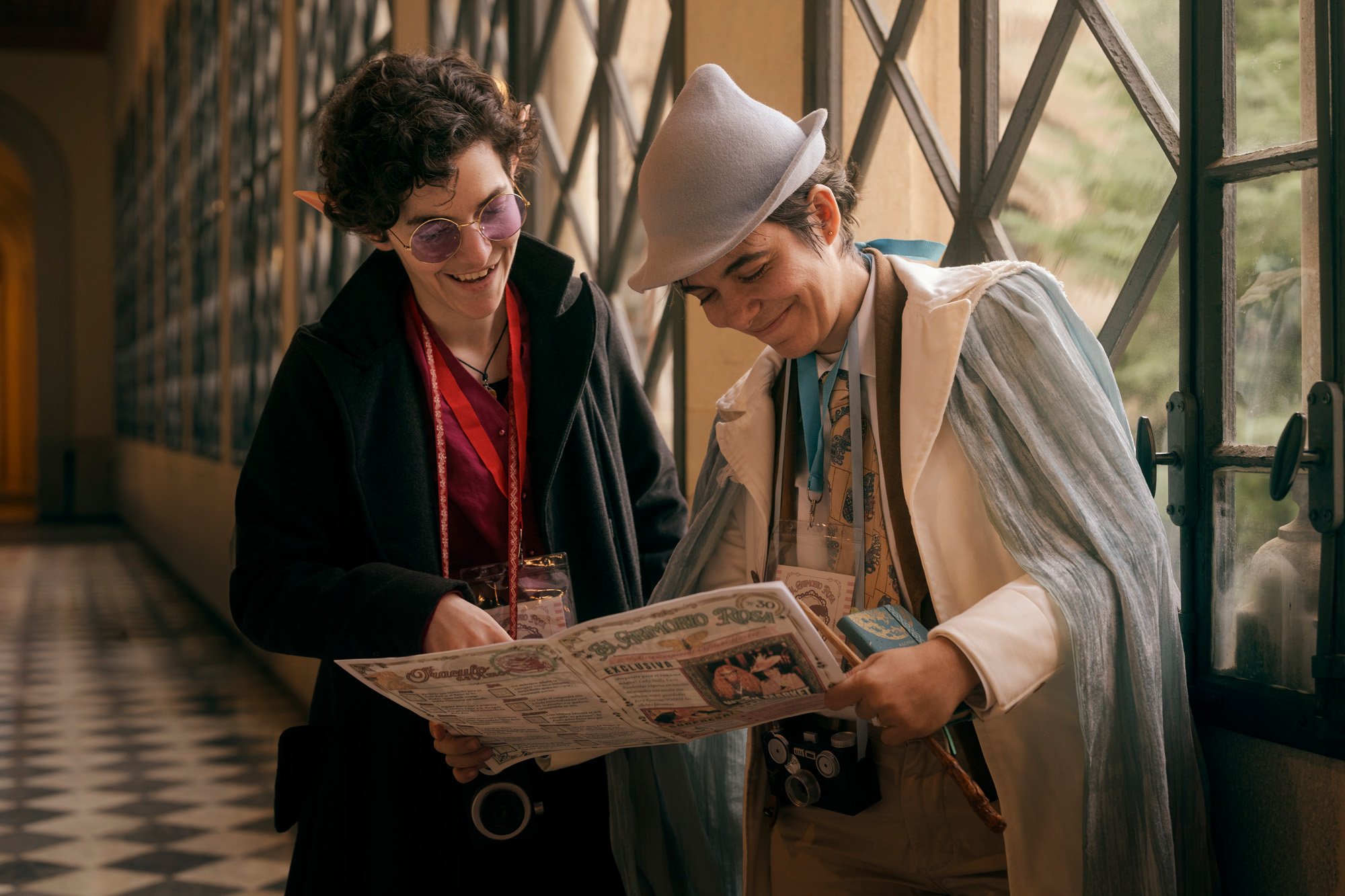 Two characters in fantasy attire reading a newspaper during the Witch Market Barcelona, captured in a candid storytelling moment.
