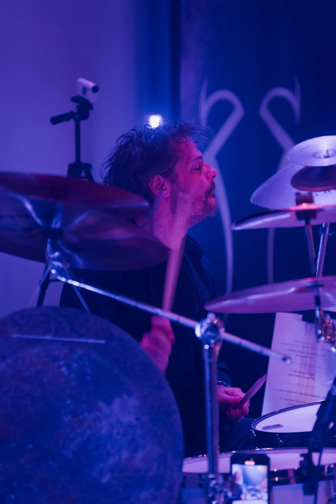 Drummer of Serapis Project performing live under concert lighting.