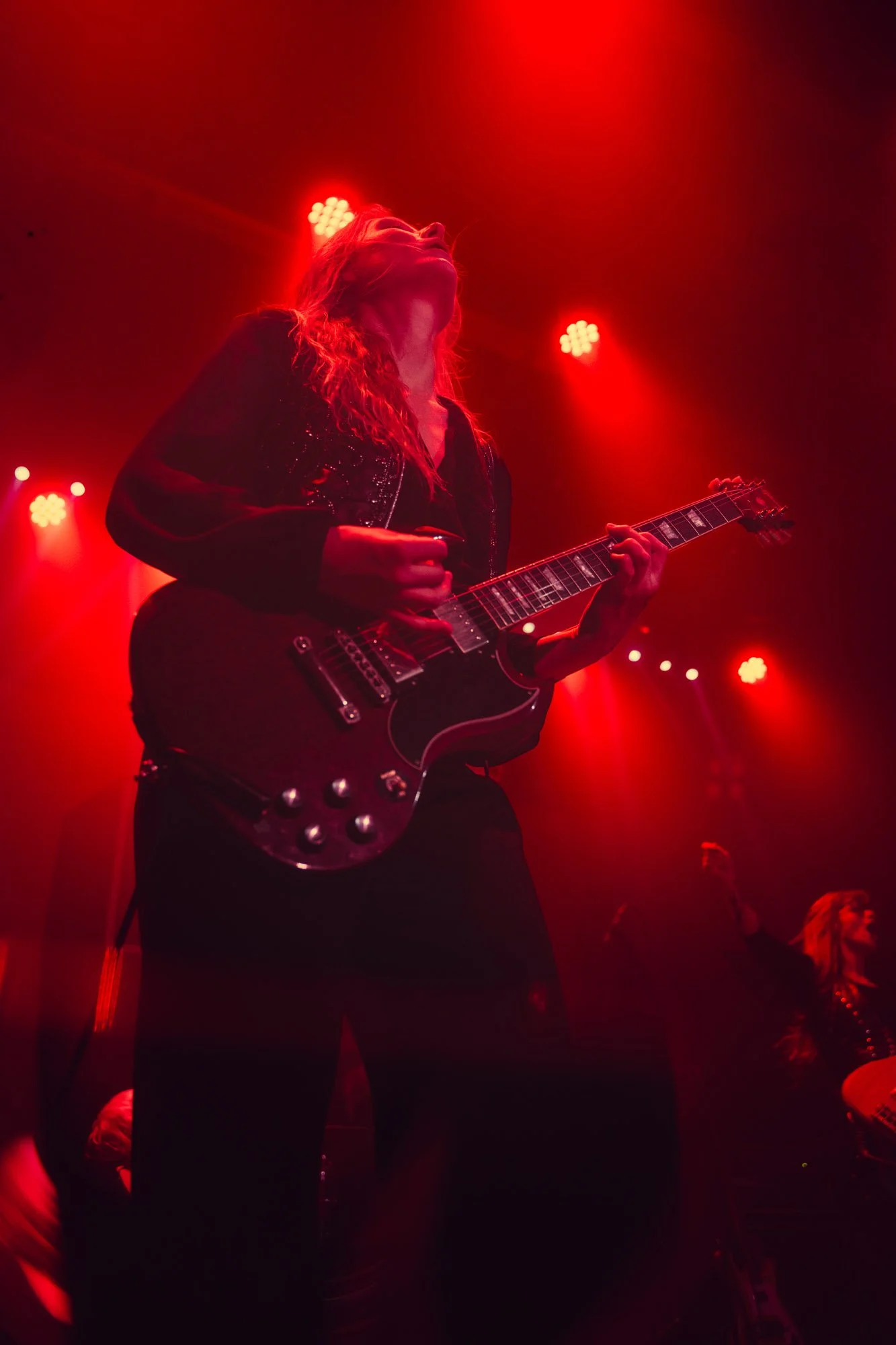 guitarist performing live with electric guitar under red lighting
