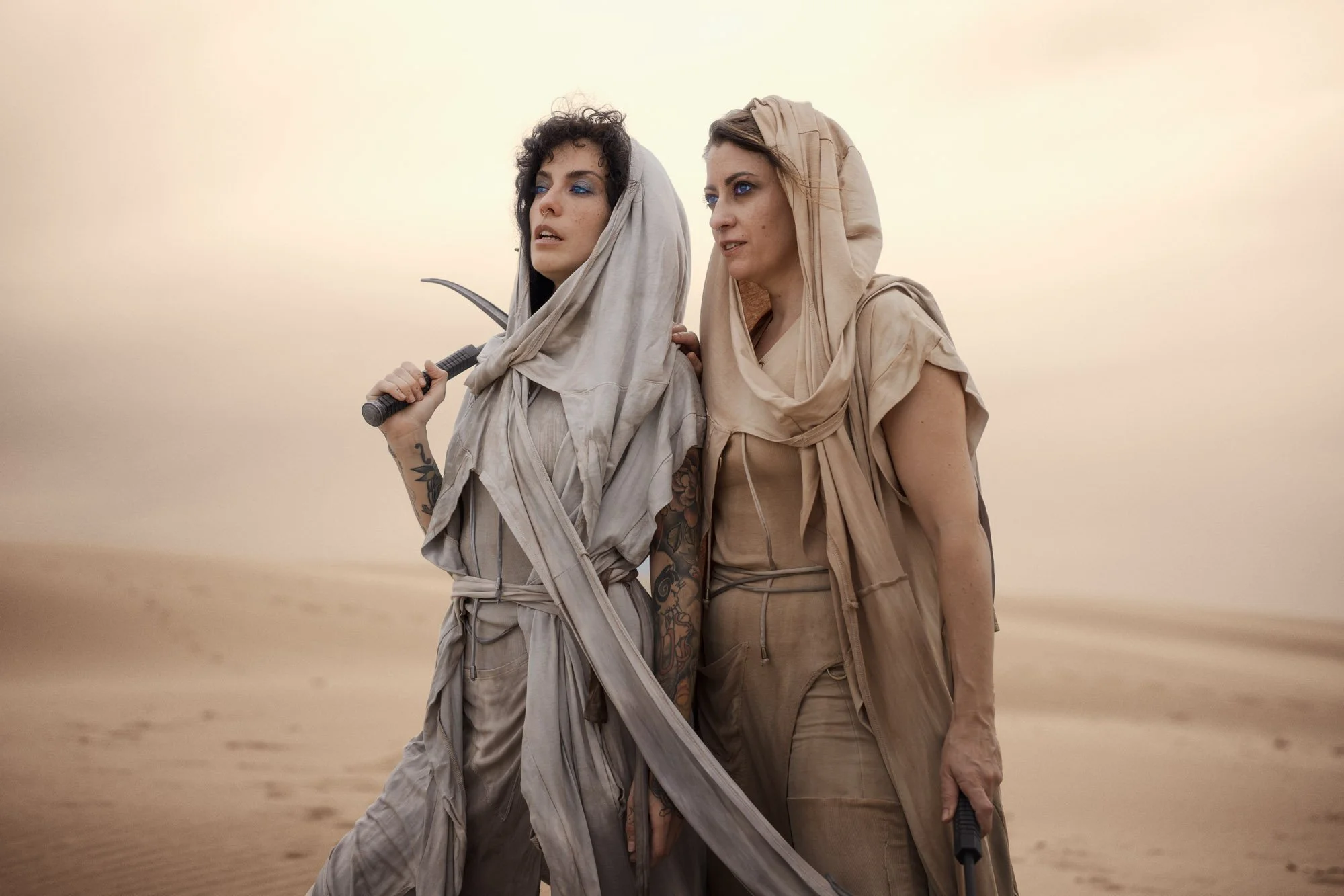 Two Fremen standing together in the desert wearing flowing Dune-inspired costumes