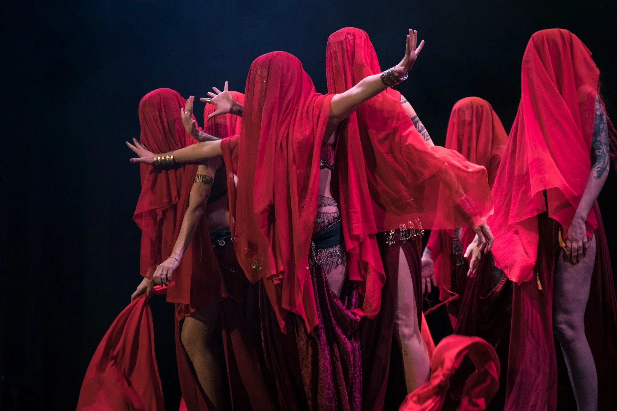 Tribal and Flames dancers performing group choreography in red veils on stage.