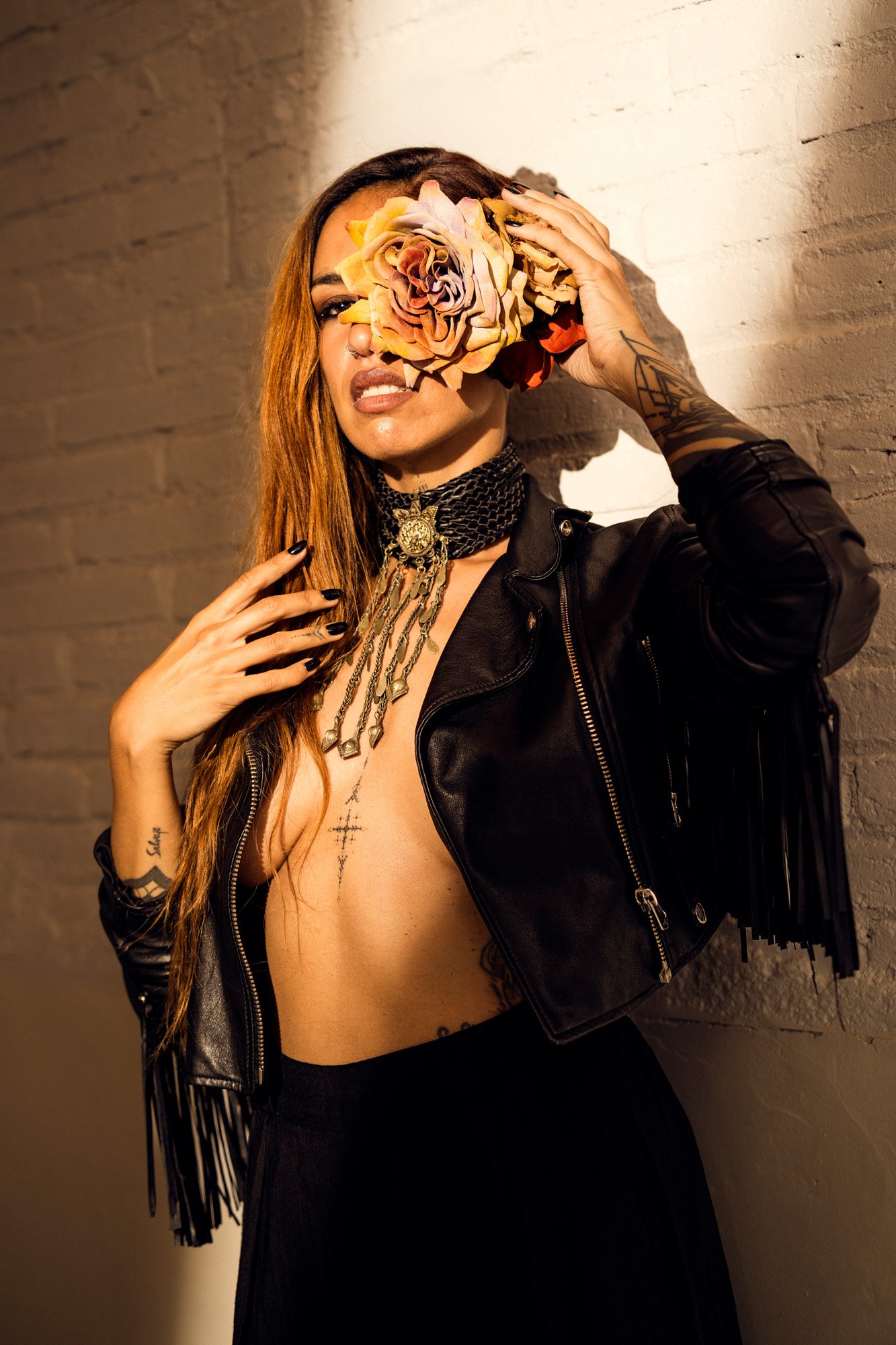 Studio fashion portrait of Nur Bloodrose with floral element and industrial styling against textured wall.
