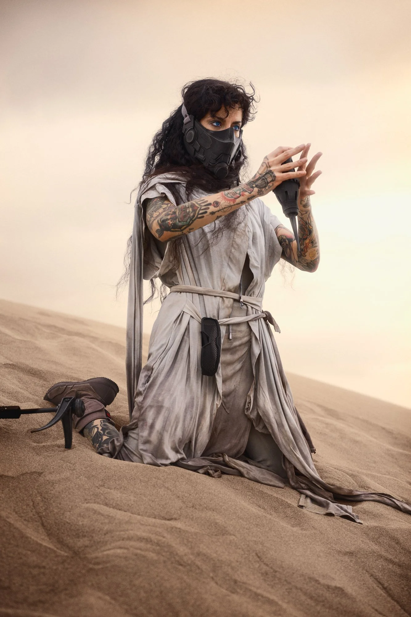 Sandra Roll kneeling in the sand as a Fremen wanderer, preparing the thumper