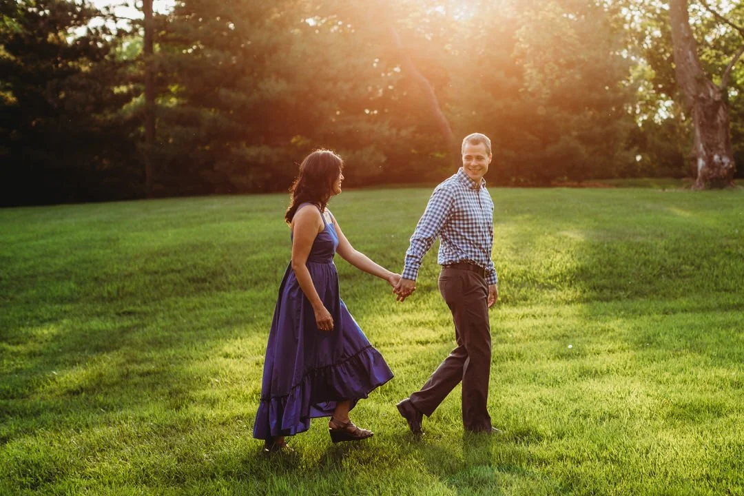man leading woman through some grass while the sun shines above them in mayslake oak brook