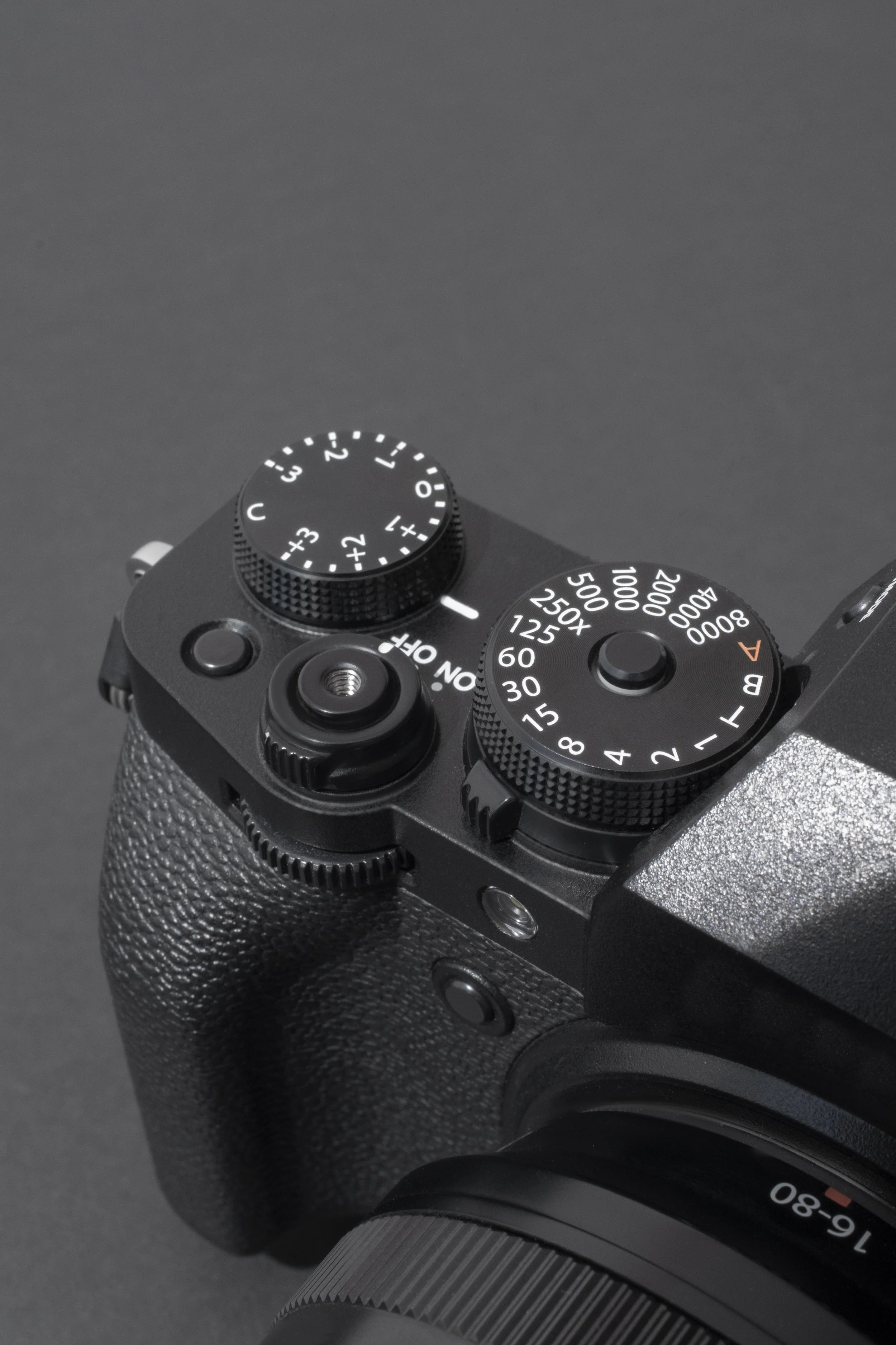 Close-up of a black digital camera showing dials and textured grip, with a large lens attached.