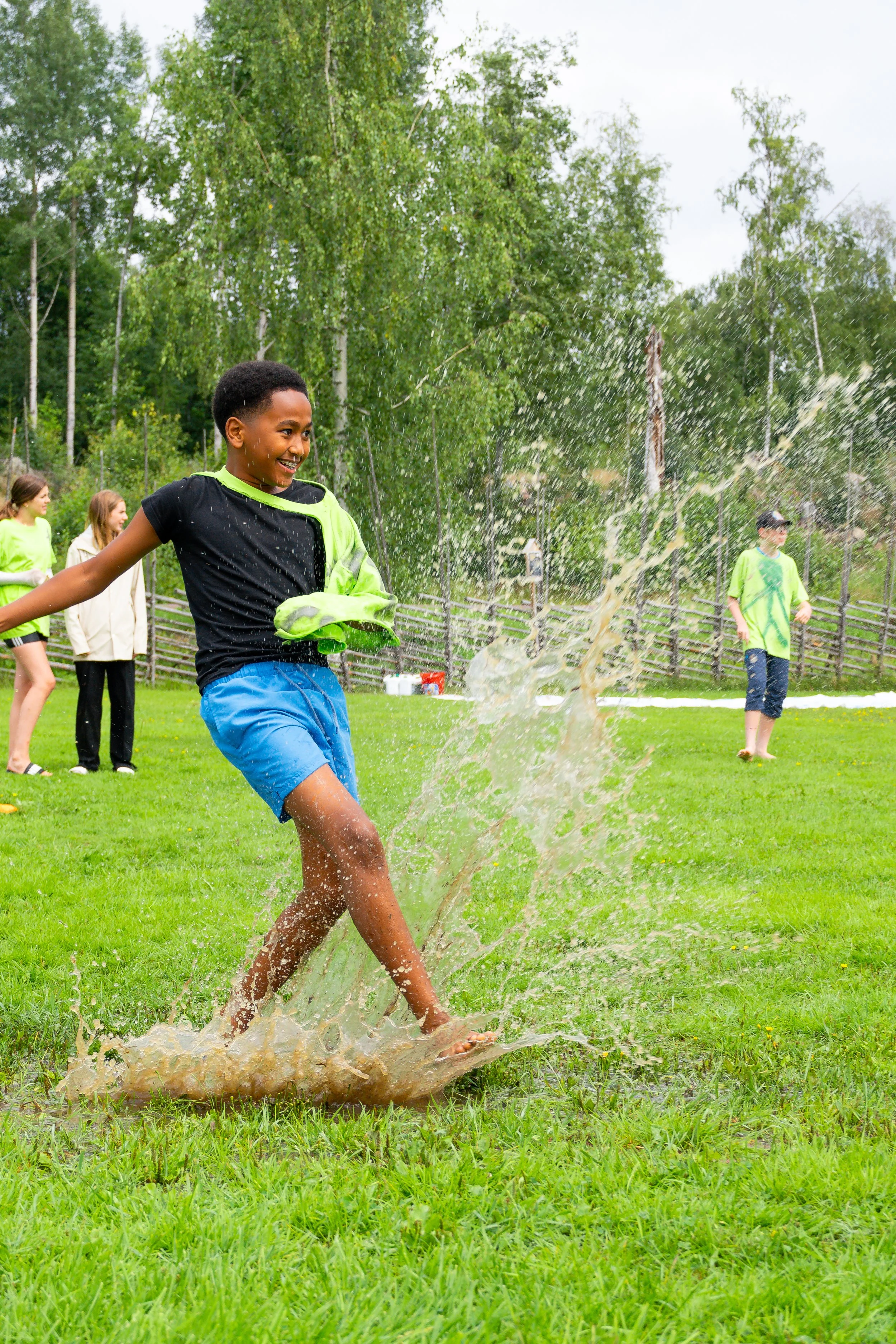 Children playing and splashing in a grassy outdoor area on a cloudy day.