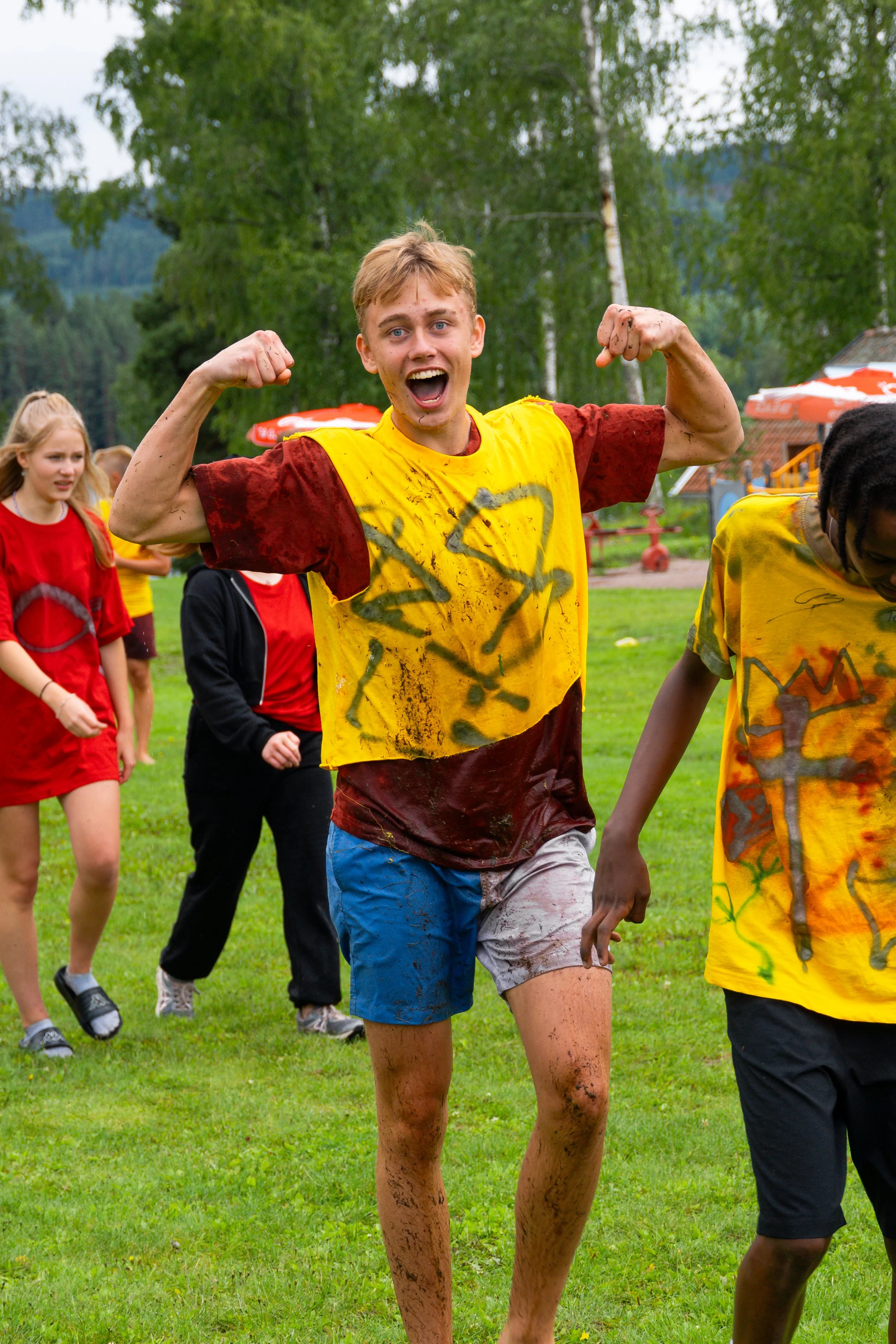 Young man celebrating outdoors with mud-stained clothes and others in the background.