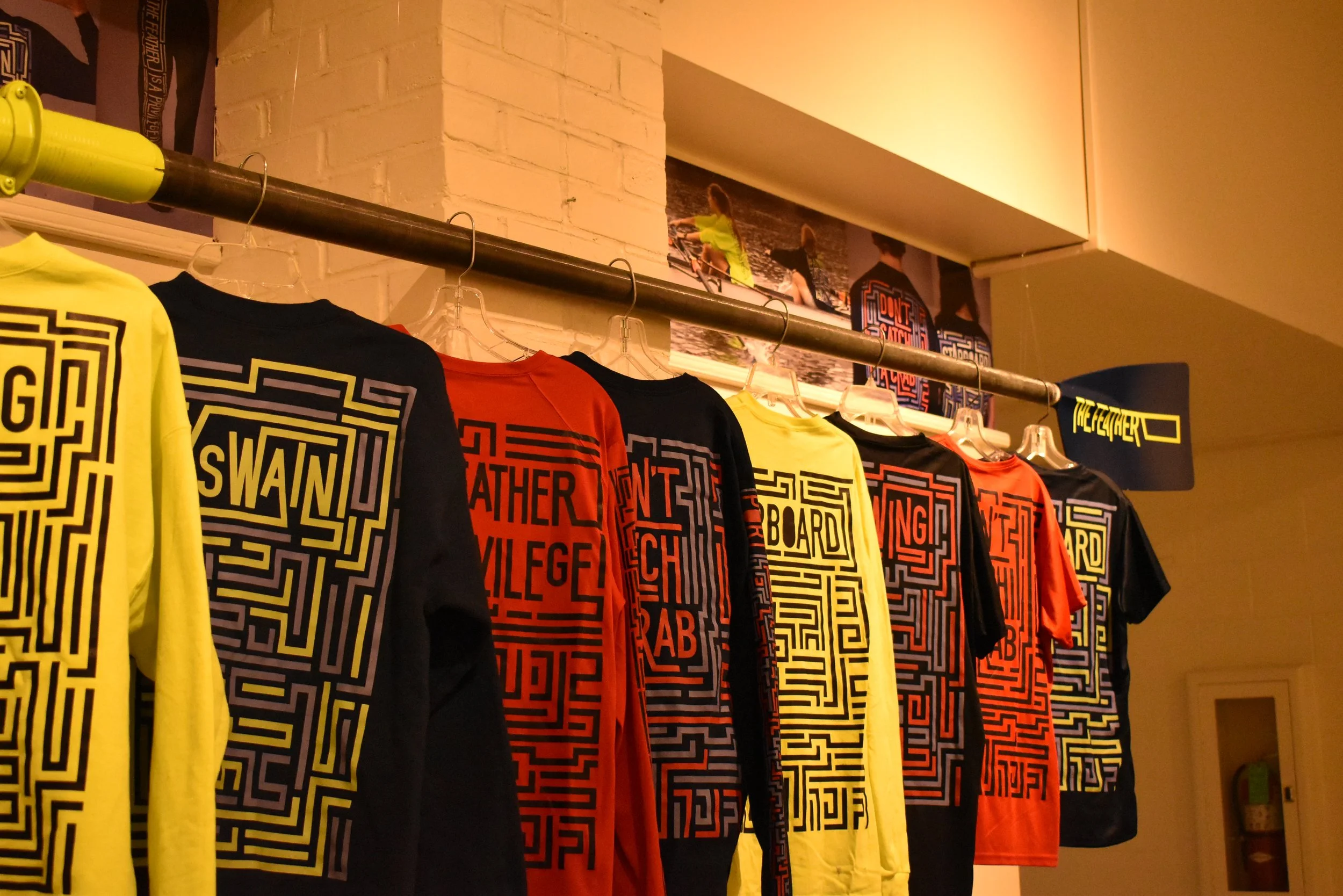 A display of colorful T-shirts hanging on a rack in a store, with a poster of children riding bikes on the brick wall above.