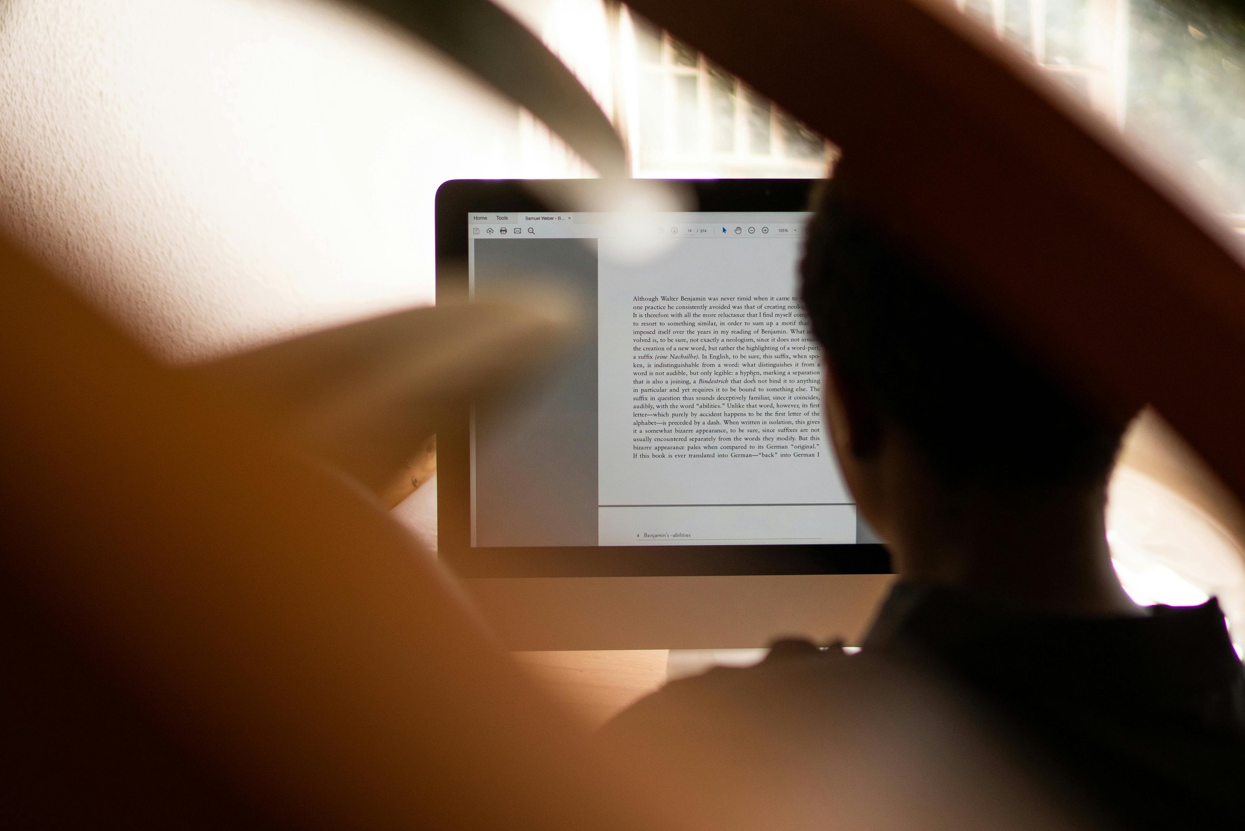 Person working on a computer, viewed through a blurry foreground with warm lighting.