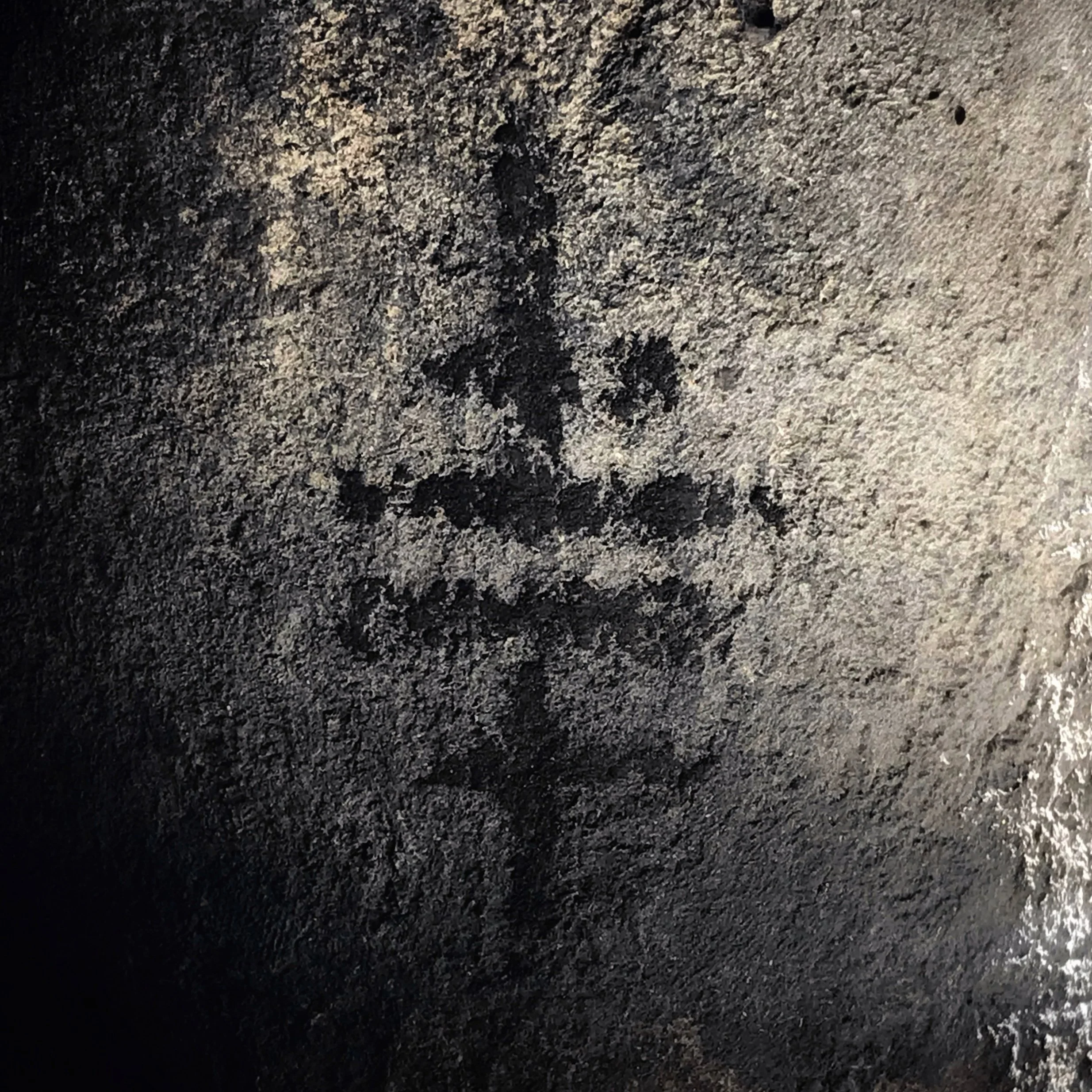 Close-up photograph of the Temple Tribe-logo drawn in charcoal on stony surface.