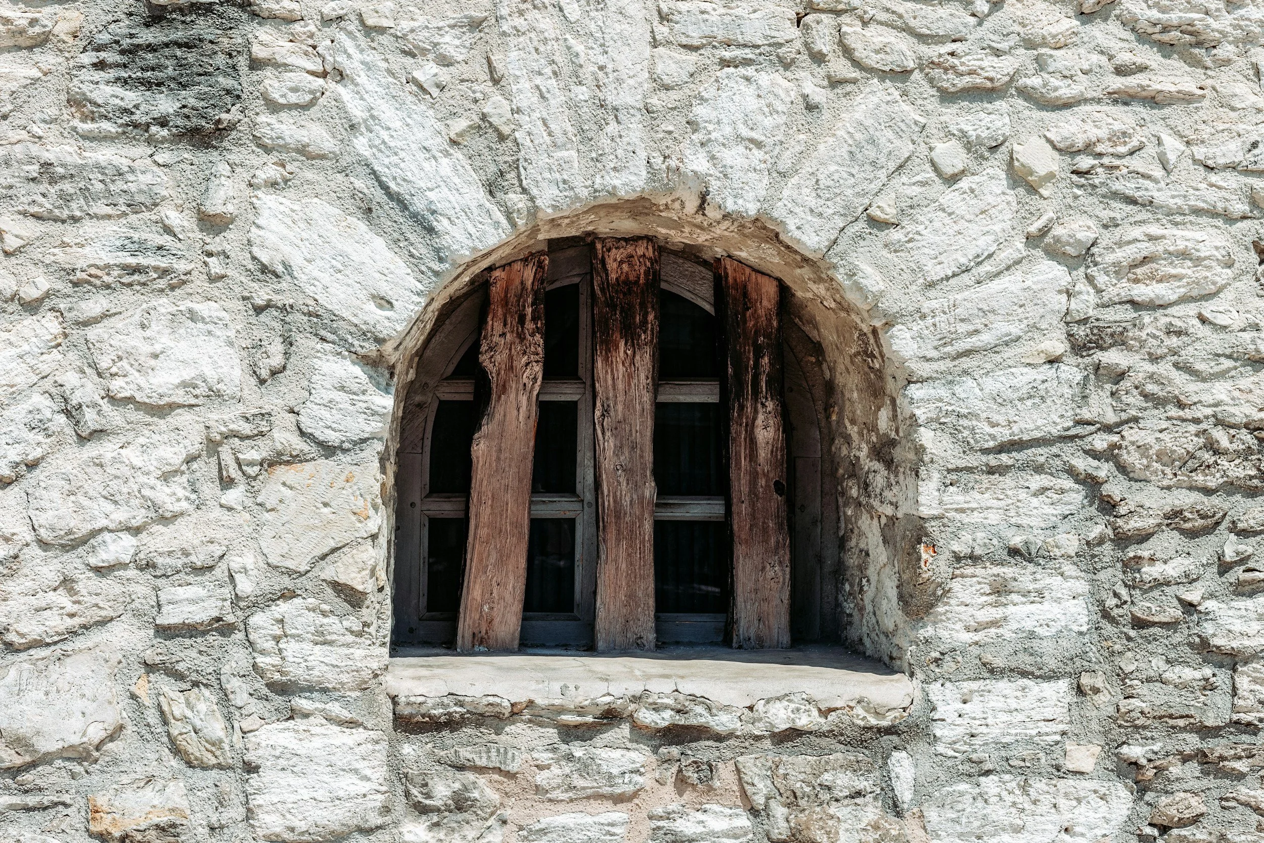 A small window in a stone wall, covered by weathered wooden planks.