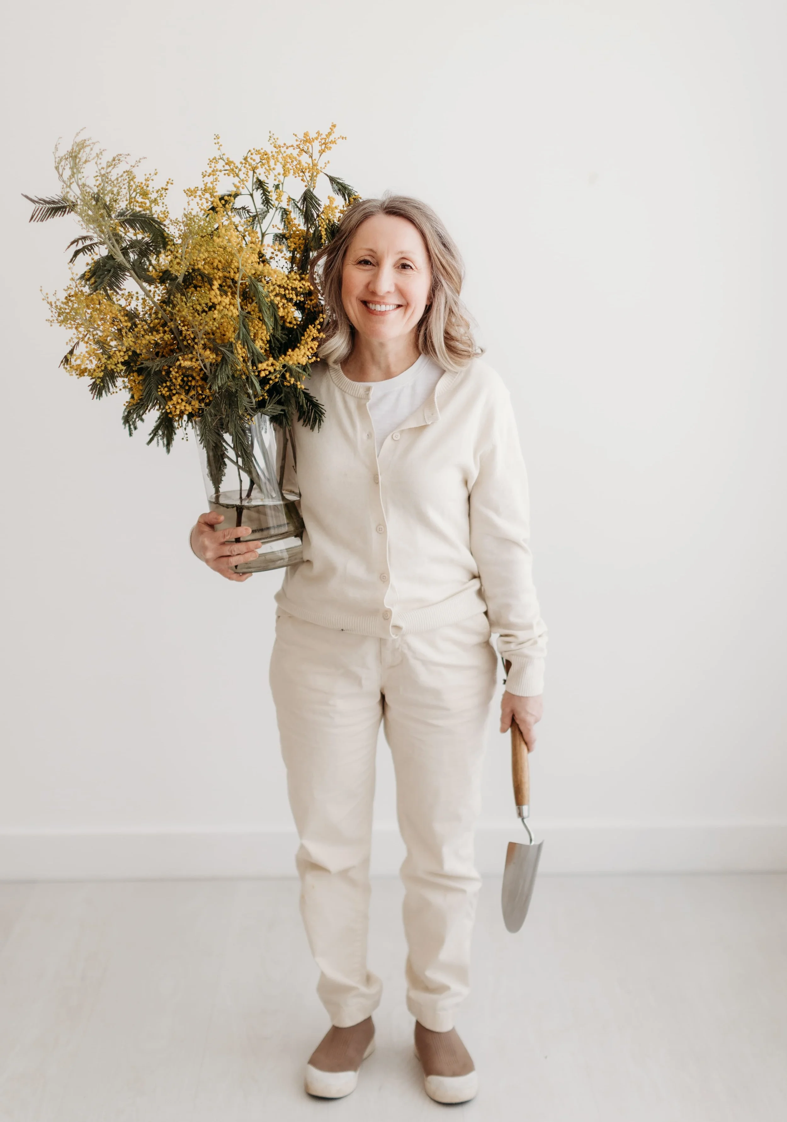 Twig & Bloom Victoria owner Ingrid holding a vase of flowers and a small gardening tool.