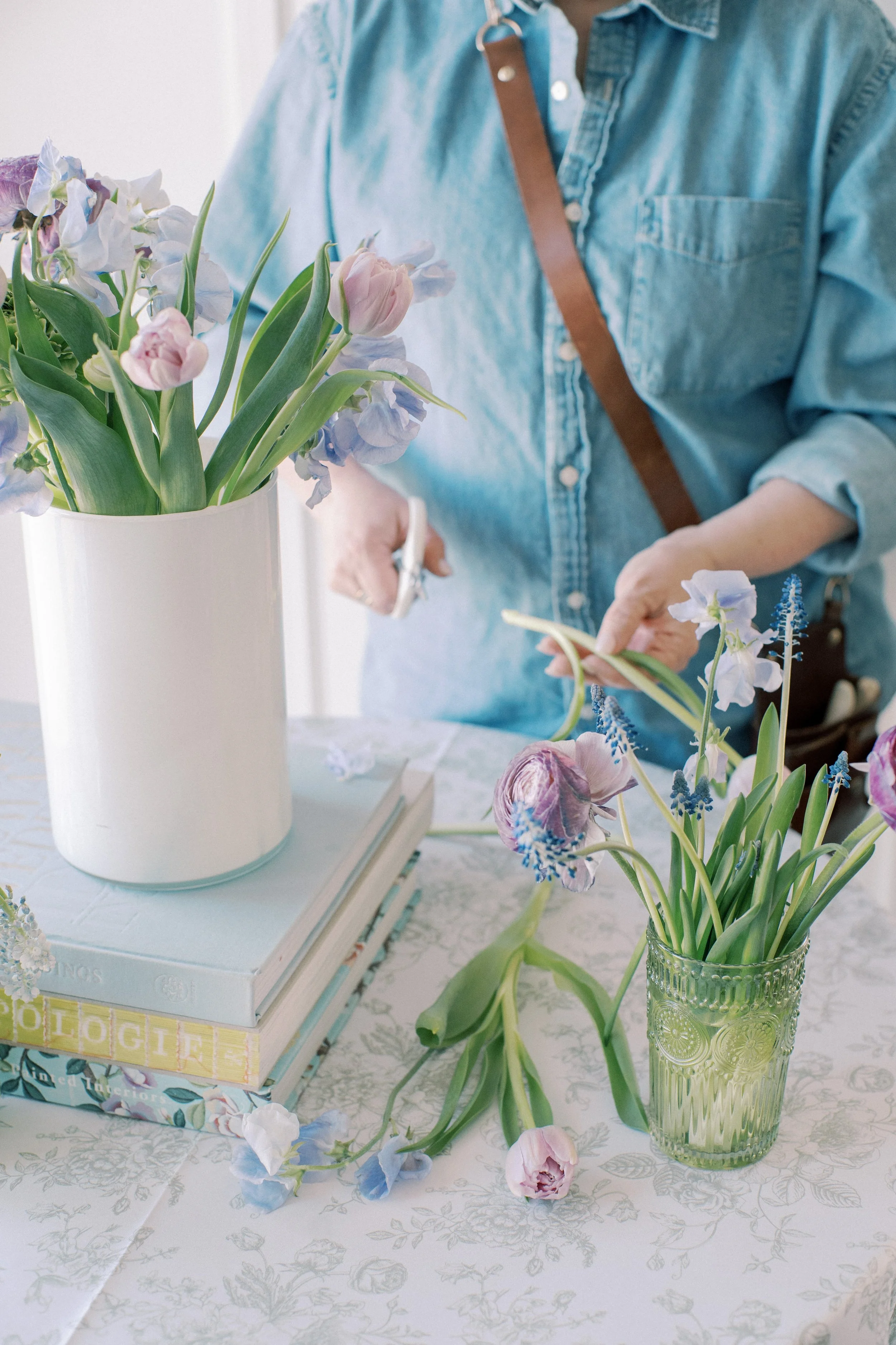 A woman standing at a table with vases of spring flowers. She is cutting the stems and preparing them to make an arrangement at a Twig & Bloom flower workshop in Edmonton, AB.