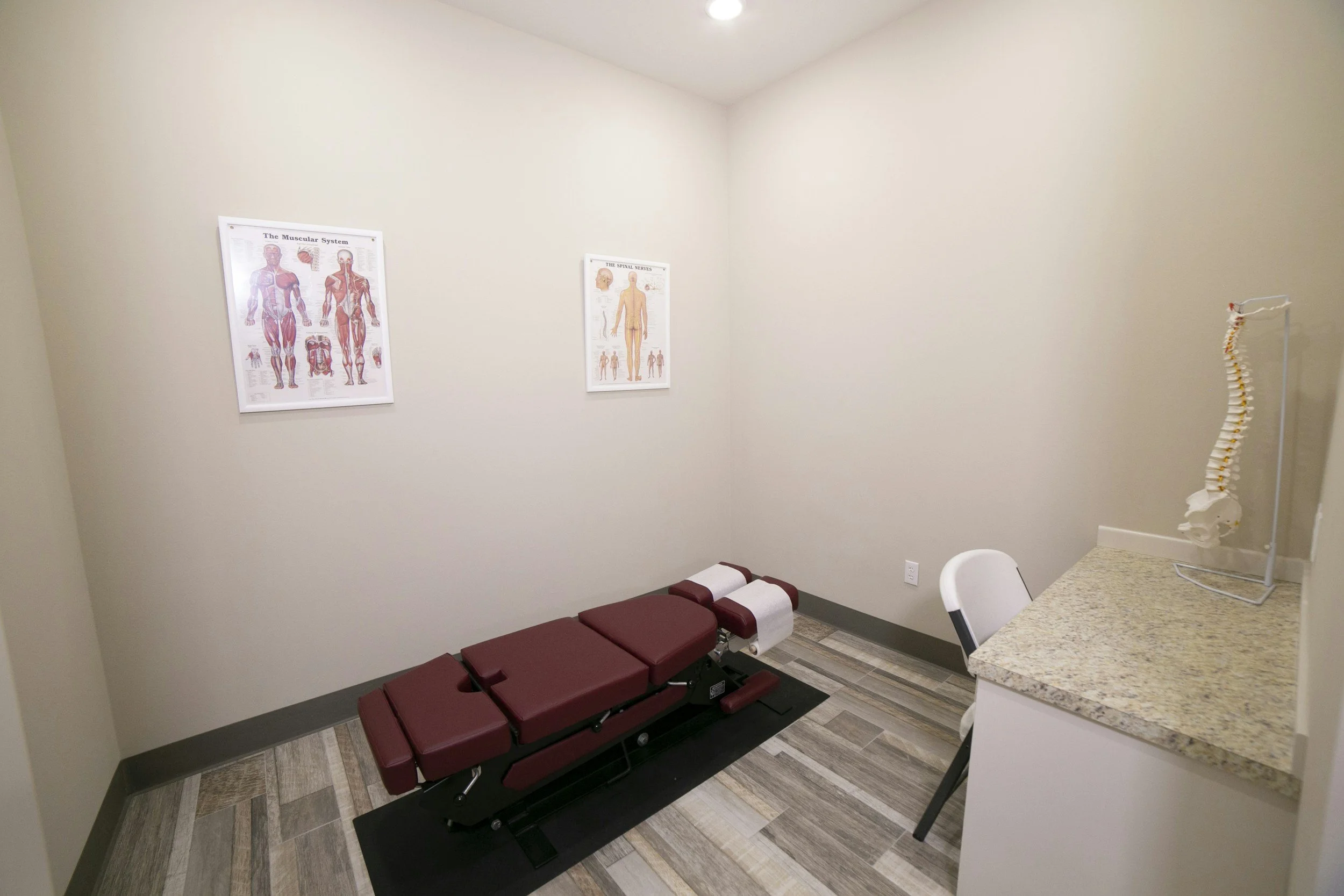 Clean medical examination room with exam table, anatomical charts, and clinical equipment