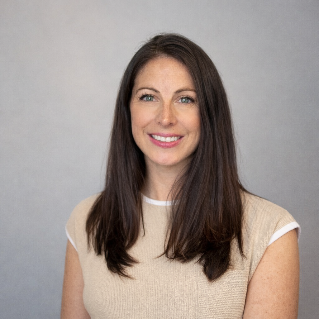 Portrait of a woman with long brown hair smiling against a gray background.